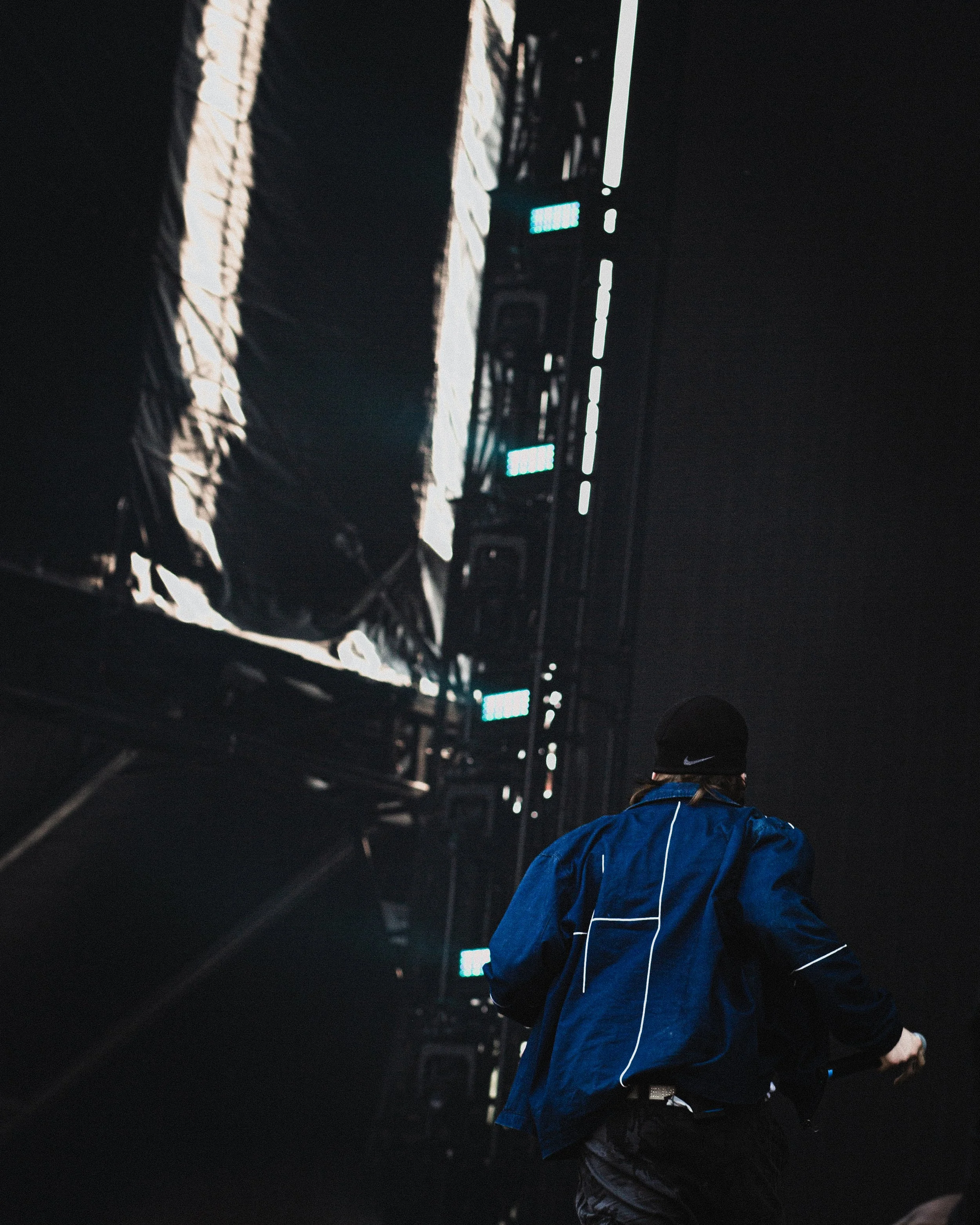 A person running outdoors near a large LED screen displaying a mostly black and white image in a dark setting