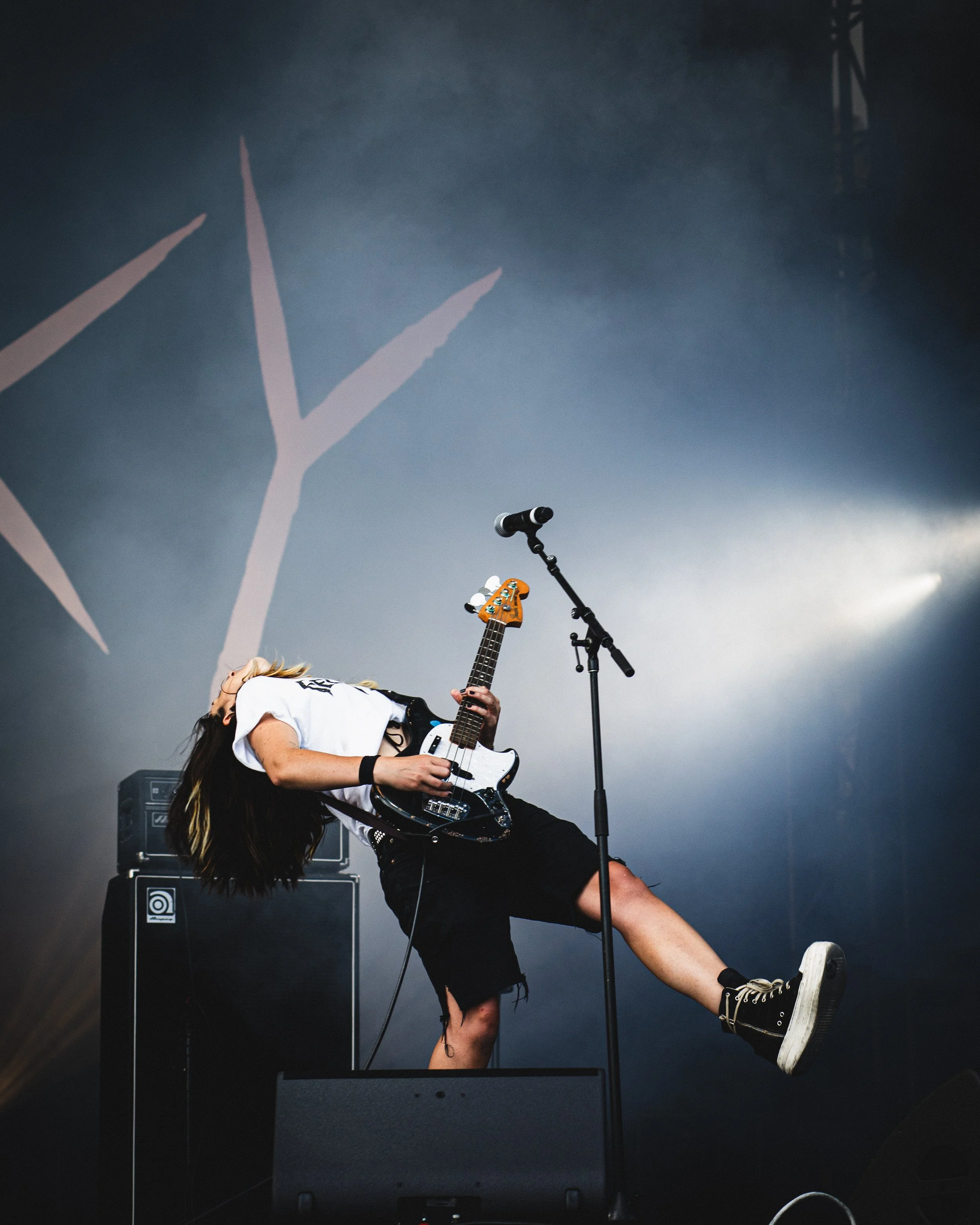 A musician playing guitar on stage with a microphone stand, amplified speakers, and stage lighting.