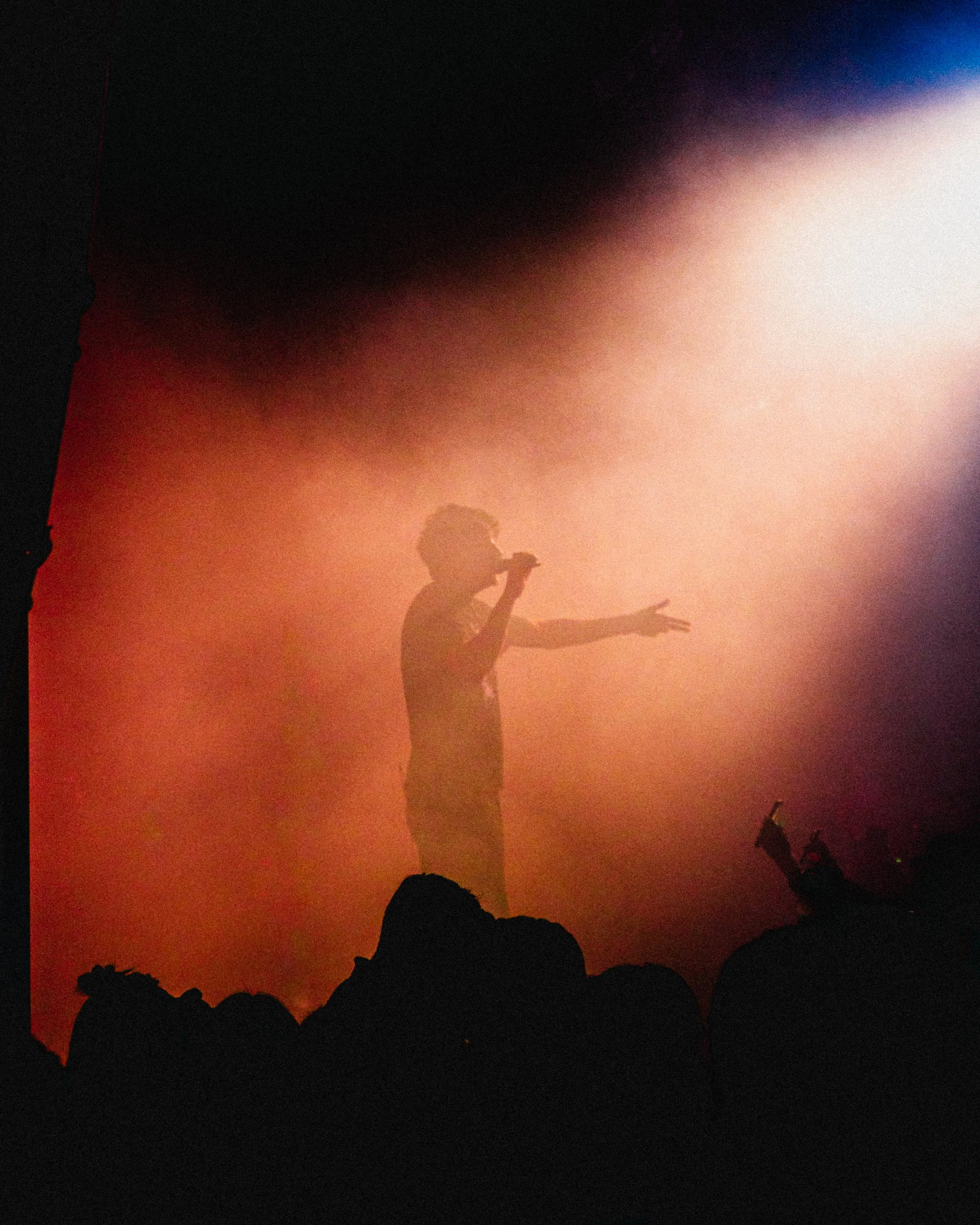 Silhouette of a performer on stage singing into a microphone with colorful stage lighting in the background.