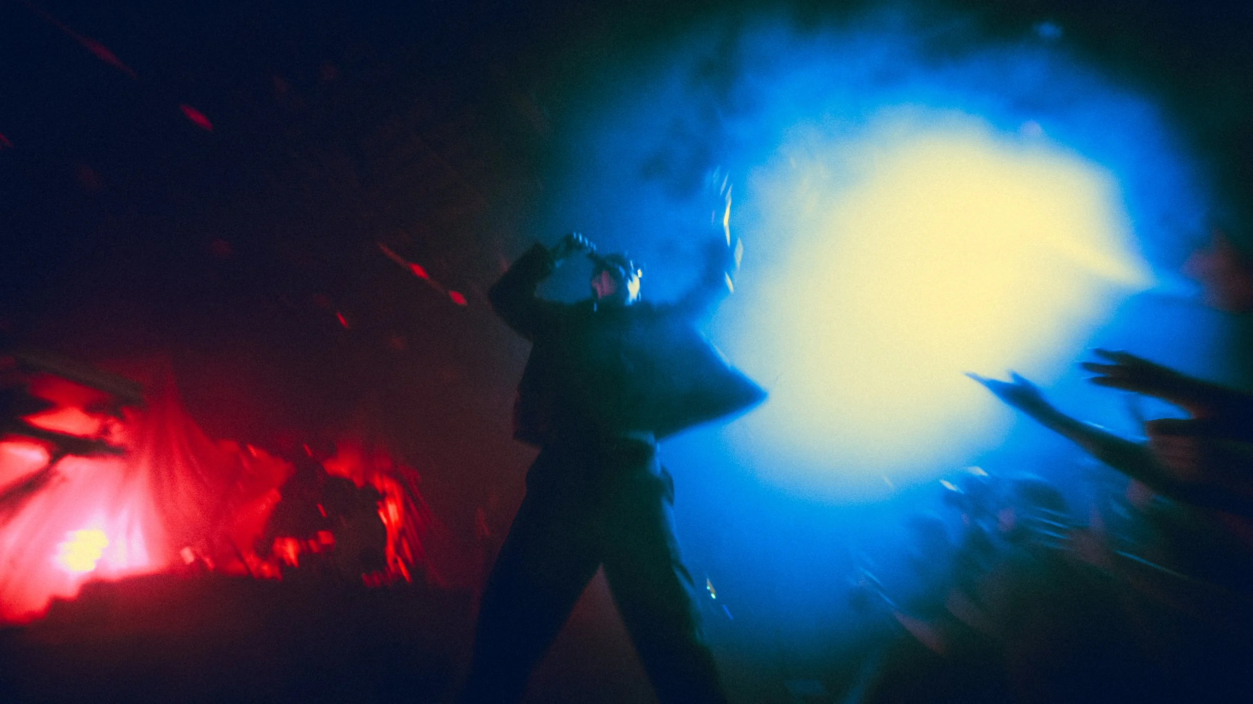 Person singing on stage with colorful red and blue lighting, raising a microphone during a concert.