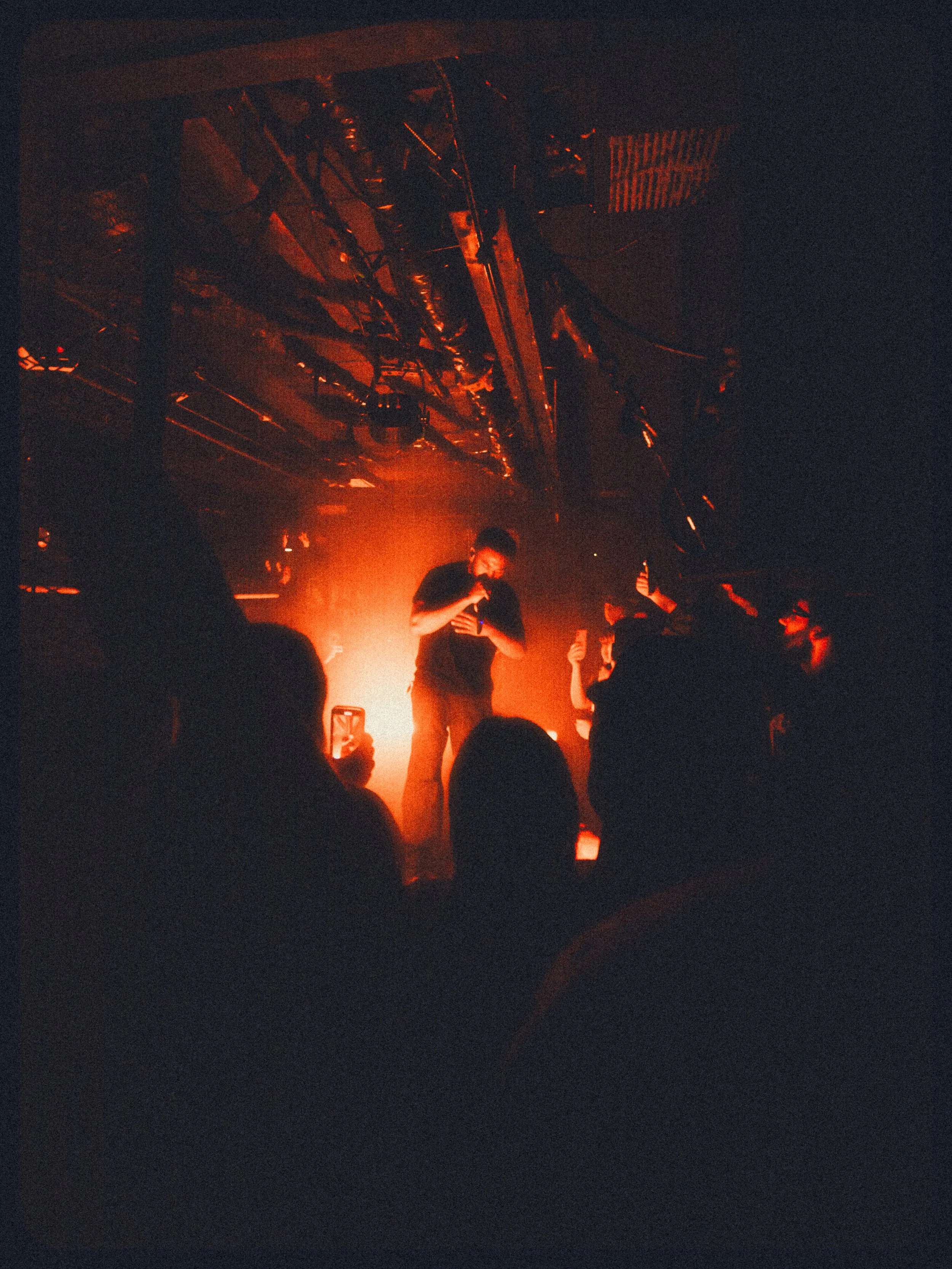 Performer singing on stage with orange lighting, audience members taking photos.