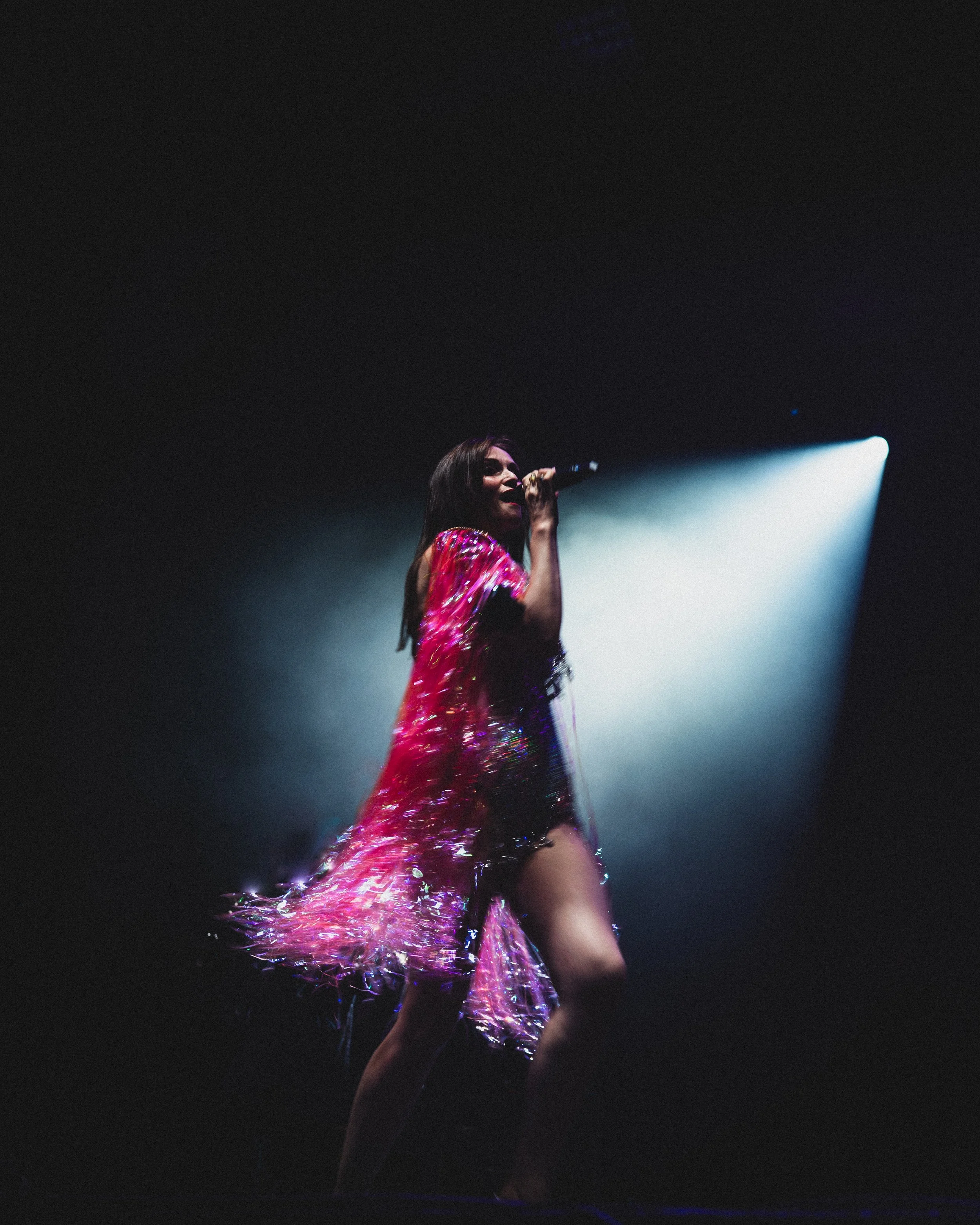 Performer singing on stage with a spotlight, wearing a bright pink, shimmery dress.