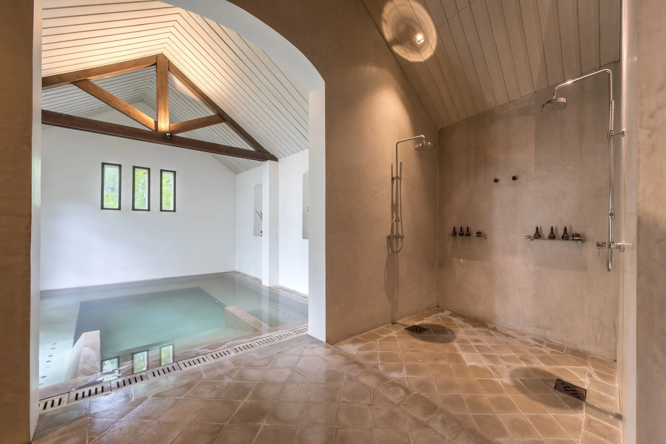 Indoor spa pool beside two showers at Amantaka, with floor drains and a tiled route between them.