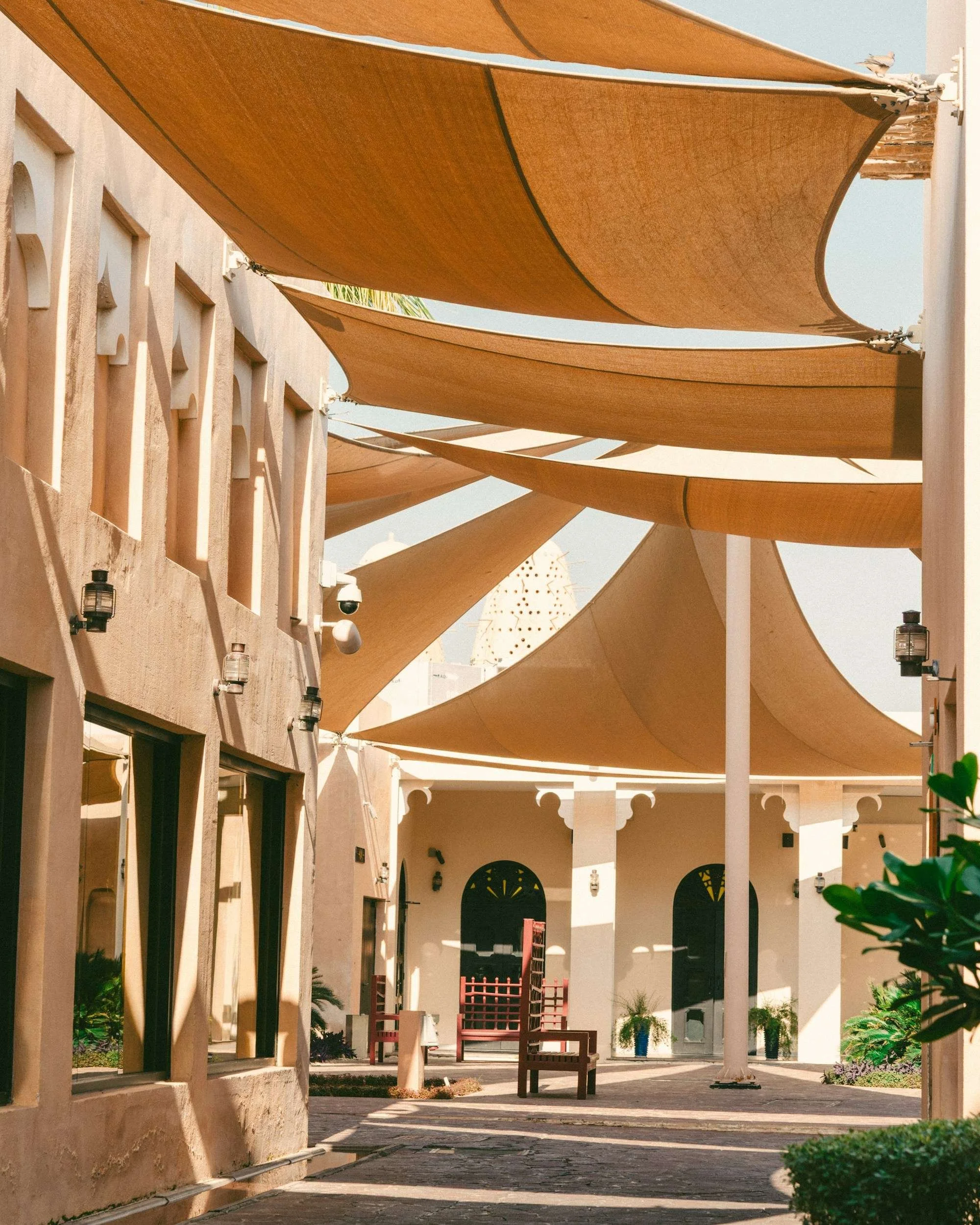 Sand-coloured fabric shade sails above a courtyard in Doha, with arched openings and seating.