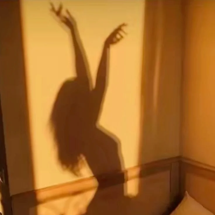 Shadow of a woman with long hair and arms raised, cast on a wall