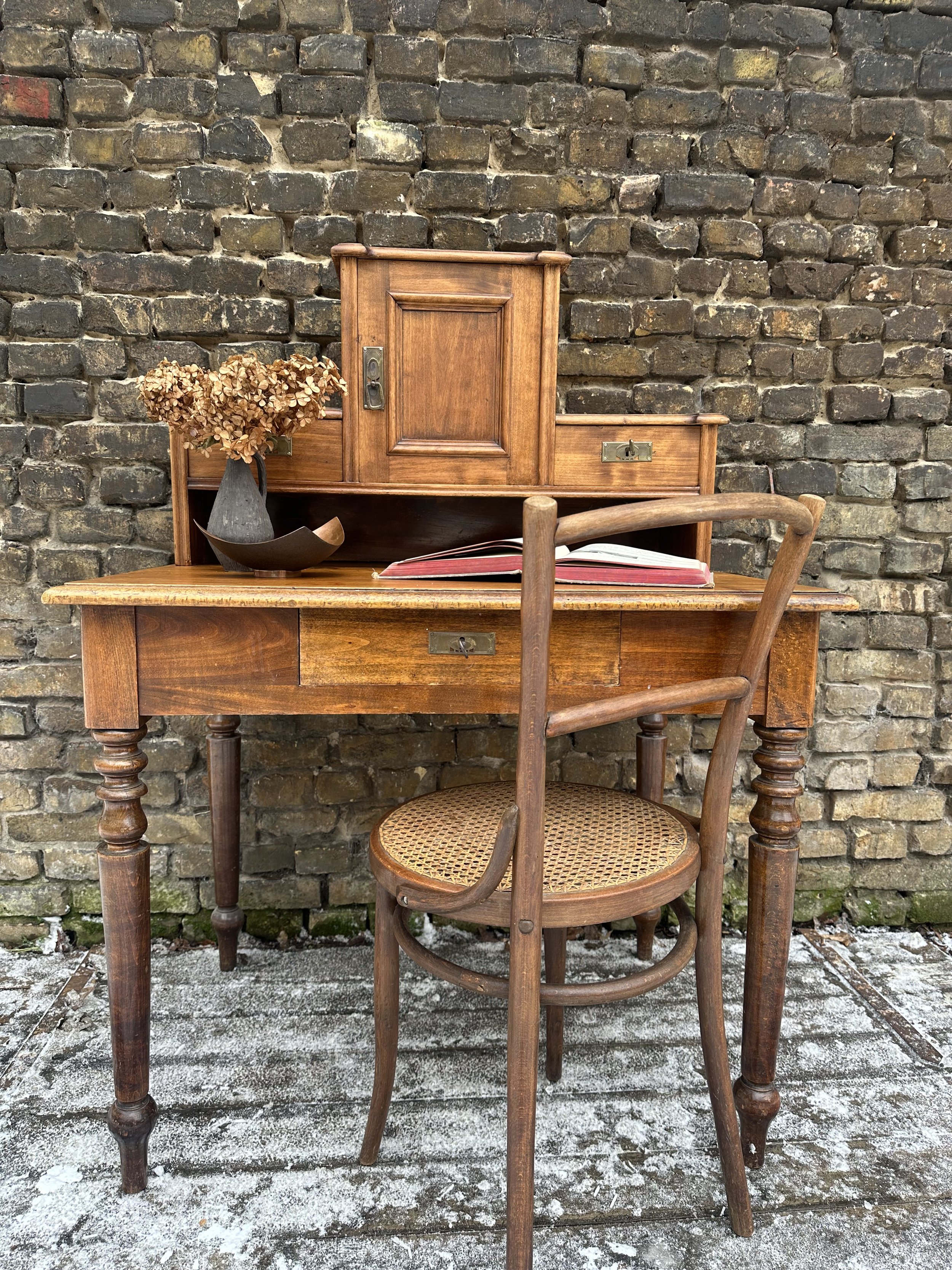 Vintage Holzsekretär mit passendem Stuhl vor Backsteinwand im Außenbereich des Stores