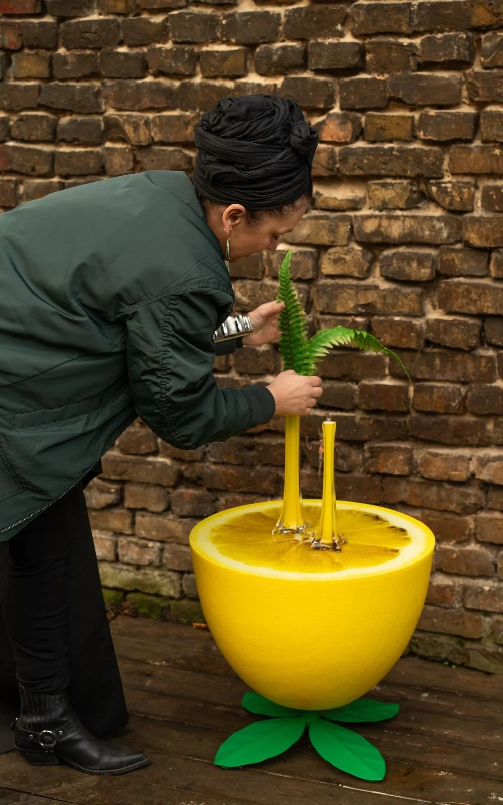 Person arrangiert grüne Zweige in gelben Vintage Vasen vor einer Backsteinwand