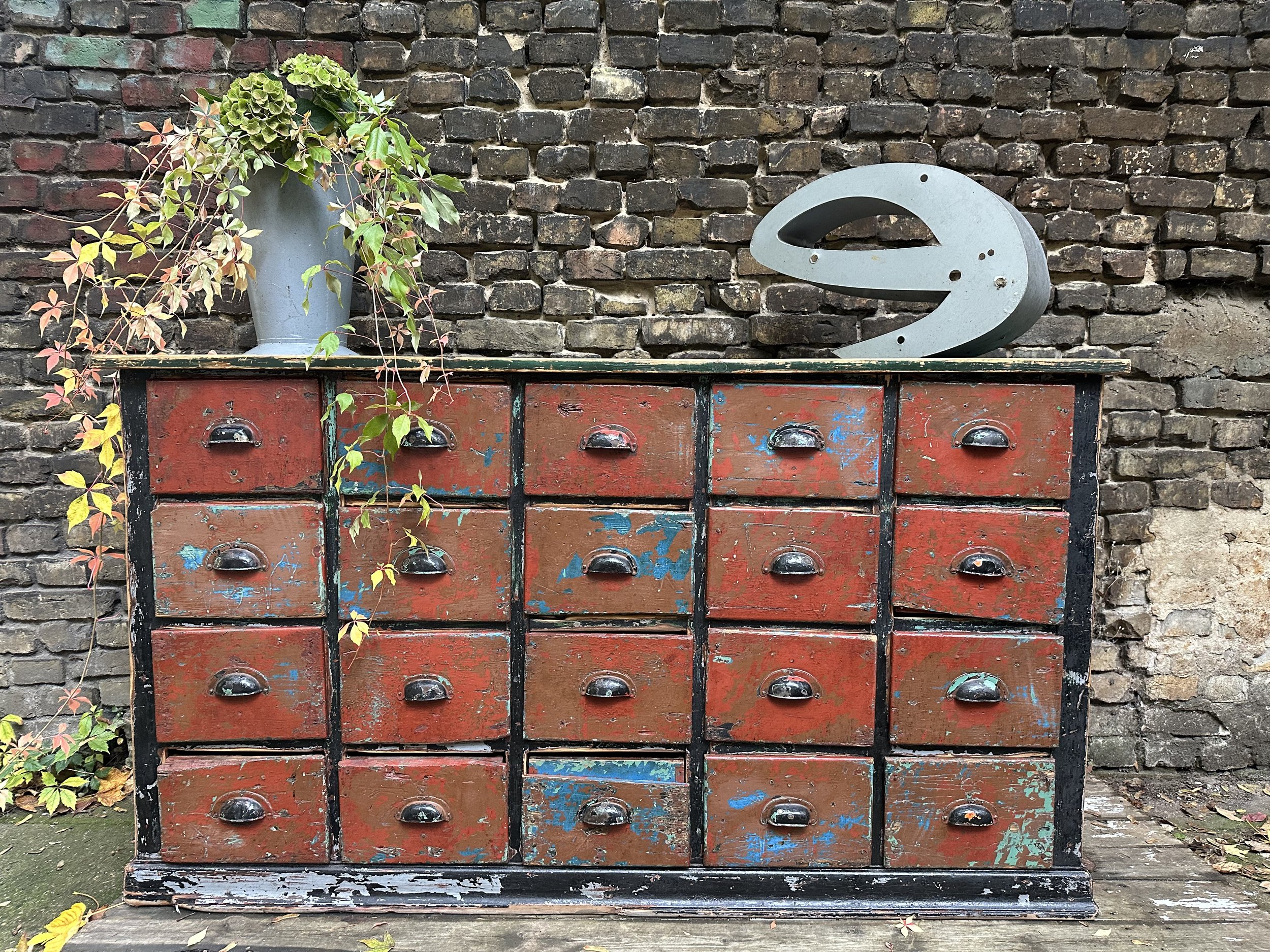 Großer Vintage Schubladenschrank aus Metall mit Patina vor Backsteinwand