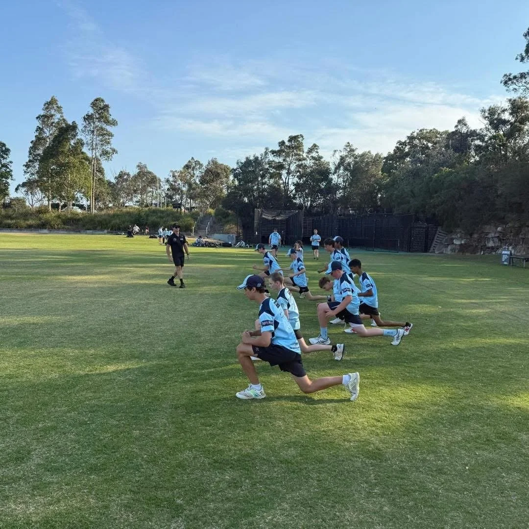 Group of young boys in sports uniforms doing stretching exercises on a grassy field.