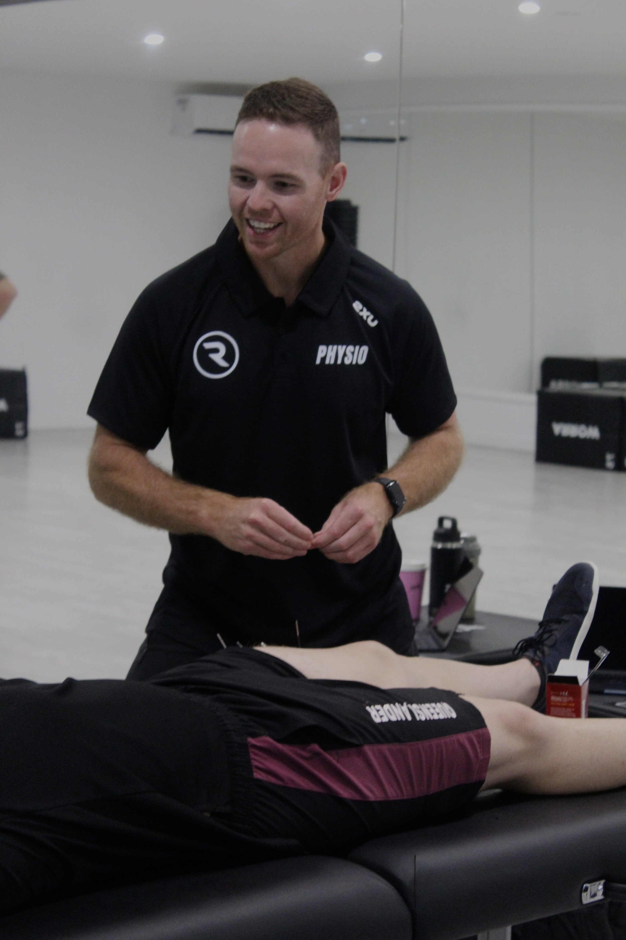 A physiotherapist provides treatment to an athlete lying on a therapy table in a fitness or physiotherapy clinic.