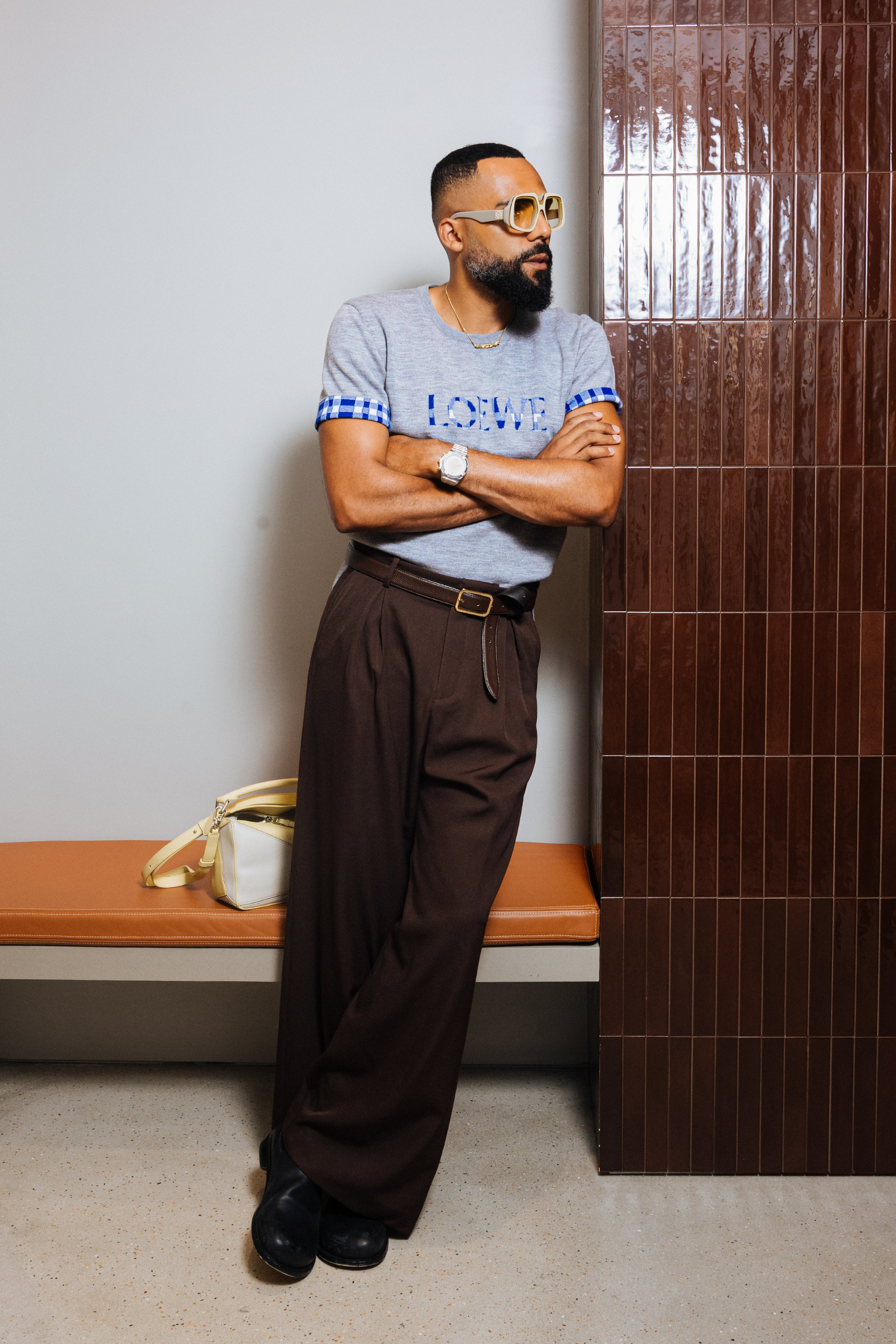 Man in sunglasses and casual clothing leaning against a wall in a waiting area.