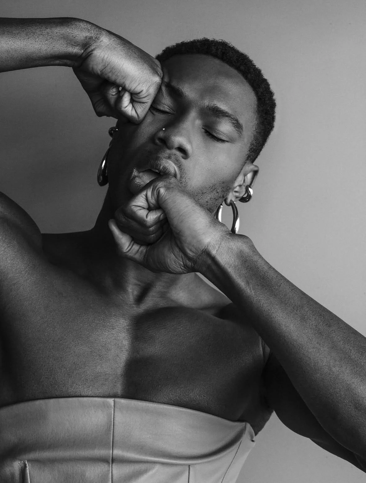 Black and white photo of a person with closed eyes, wearing earrings, with their hand near their face, showcasing a contemplative expression.
