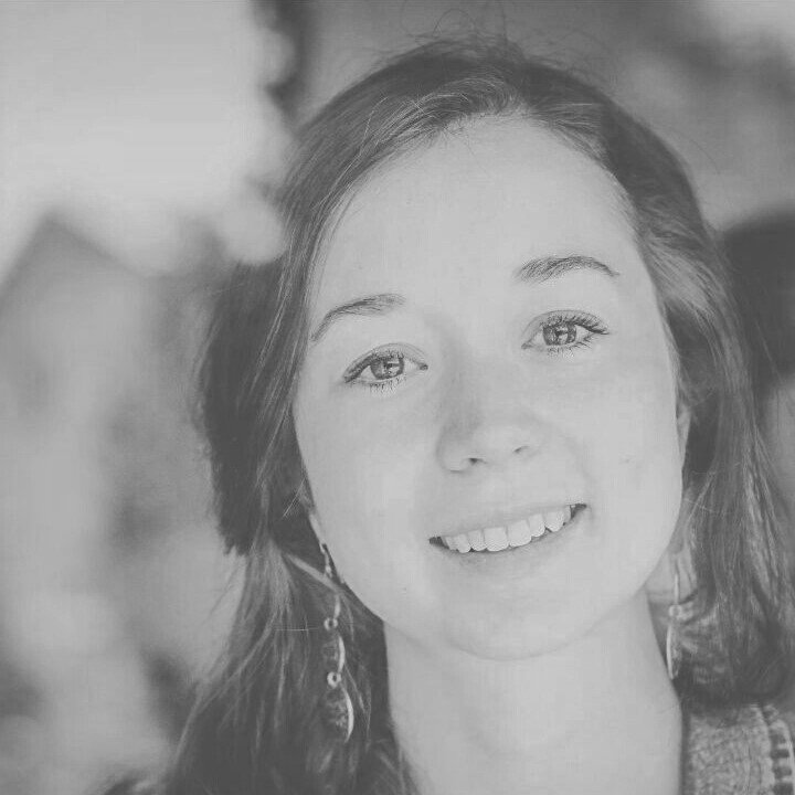 Nahaufnahme eines Lächelnden jungen Mädchens mit langen, lockigen Haaren und Ohrringen, in Schwarz-Weiß.