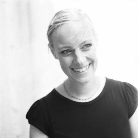 Schwarz-weiß-Foto einer lachenden Frau mit kurzen blonden Haaren, die eine schwarze T-Shirt trägt.