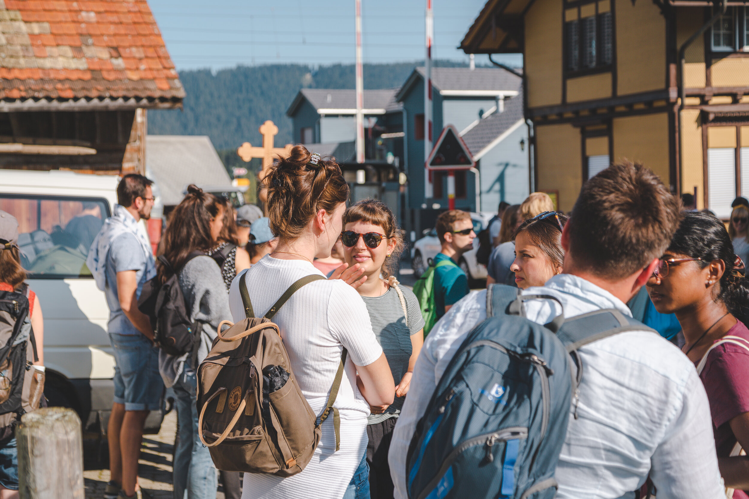 Menschen versammeln sich auf einer Straße in einer kleinen Stadt, einige mit Rucksäcken, beim Tagesausflug oder einer Gruppenreise.