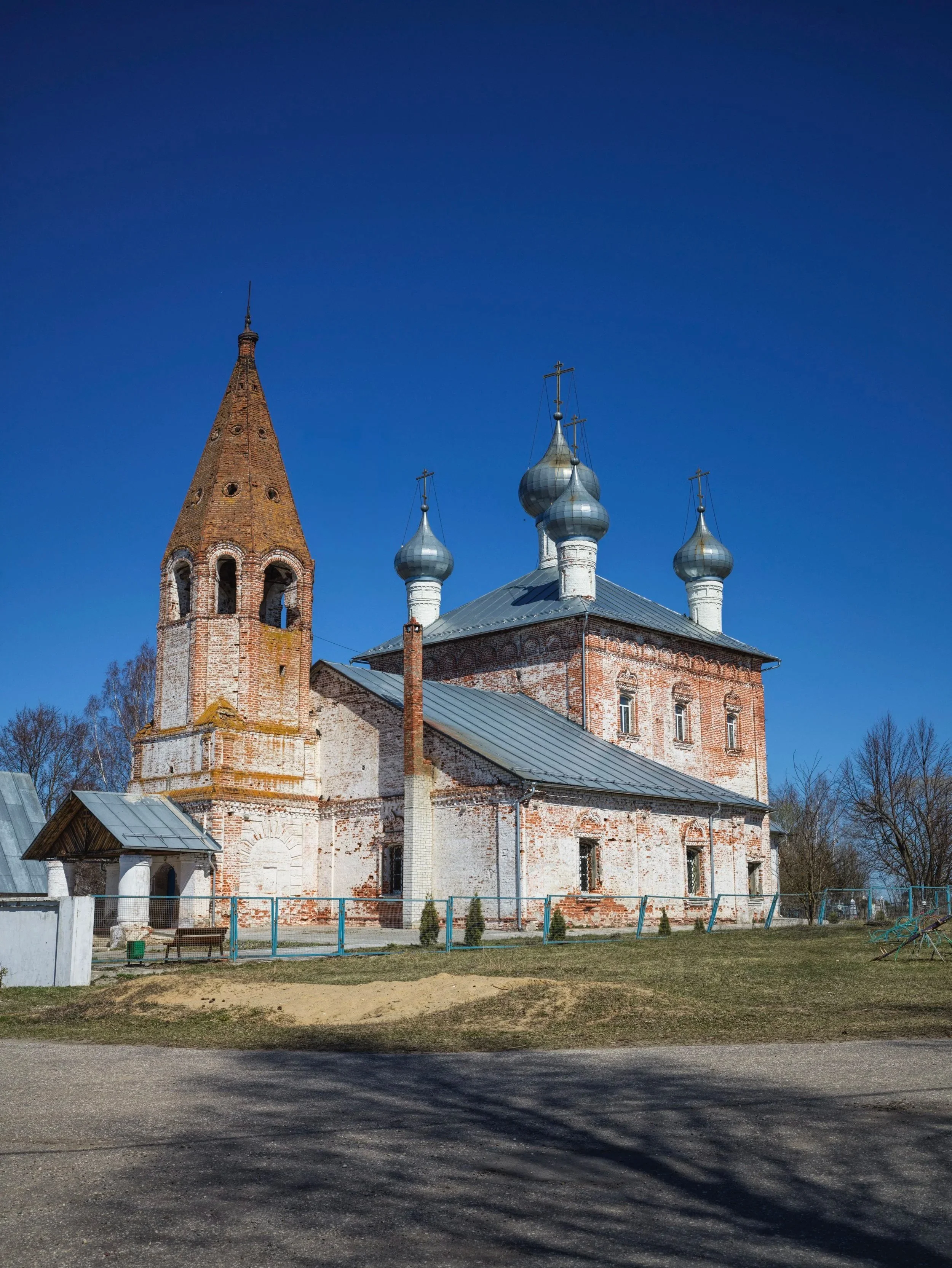 A historic brick church with three metal onion domes and a tall brick bell tower against a clear blue sky.