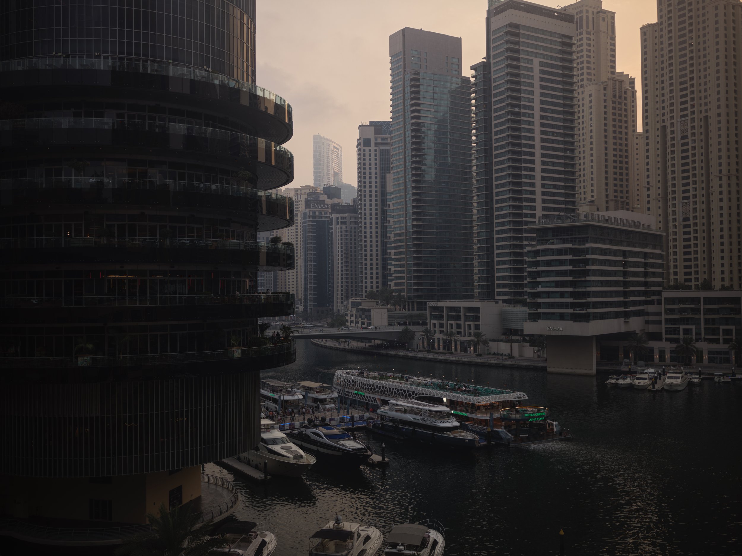 Cityscape of modern high-rise buildings around a marina with yachts and boats, under a cloudy sky.