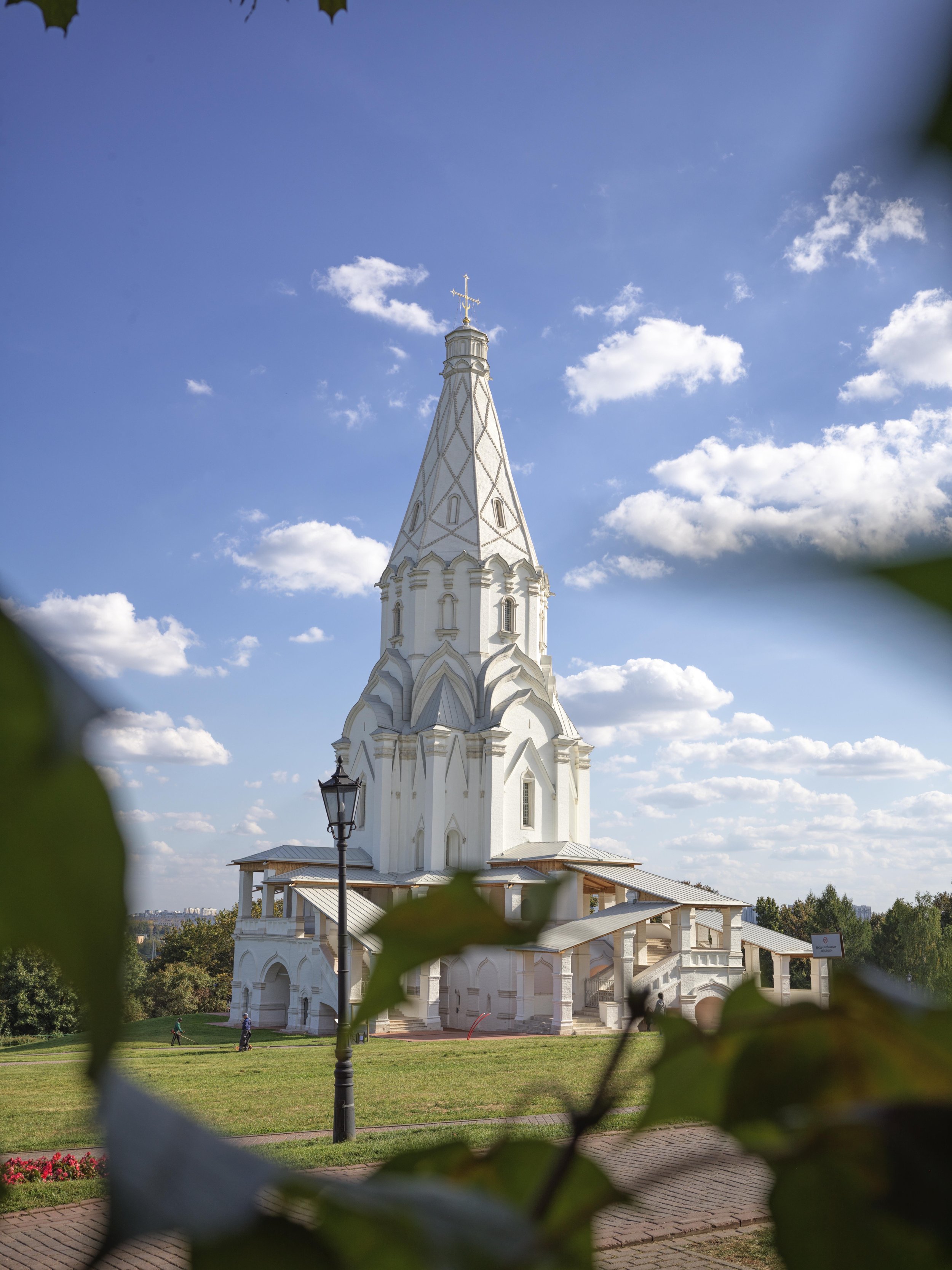 A white church with a tall steeple, surrounded by green grass and trees, under a blue sky with scattered clouds.