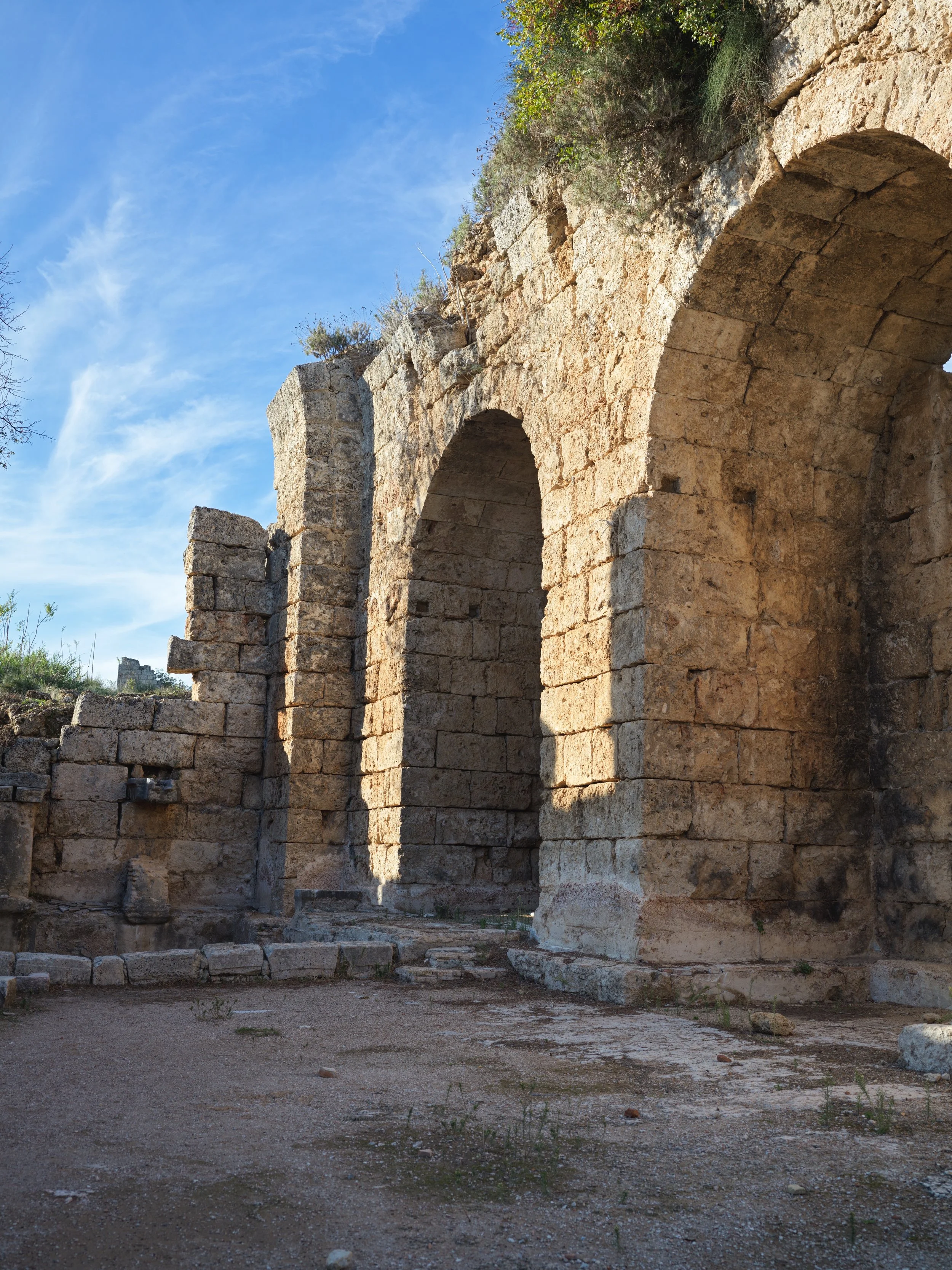 Ancient stone ruins with large arches and partially collapsed walls, set against a bright blue sky