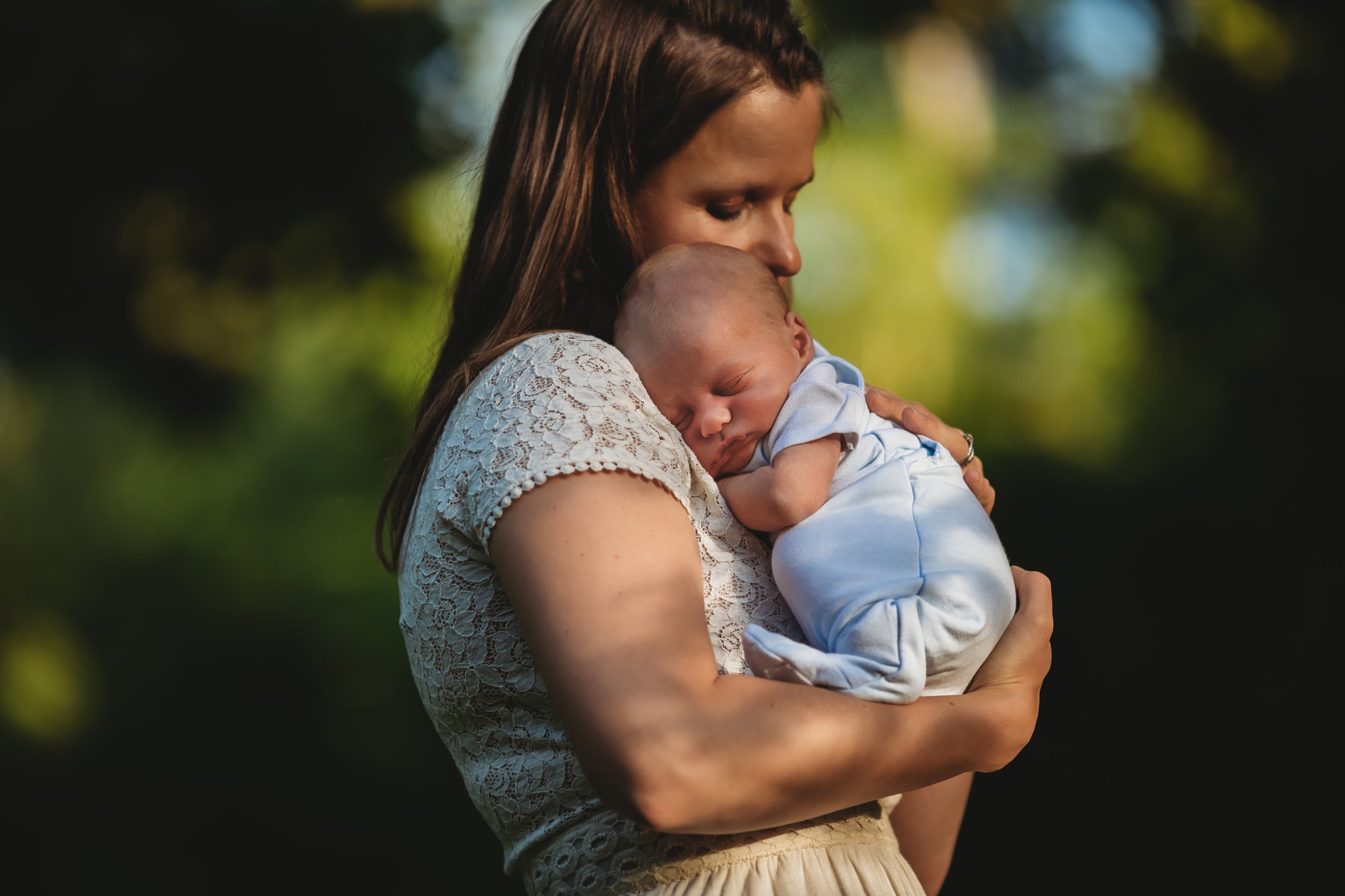 A woman holding a sleeping baby outdoors during daytime.