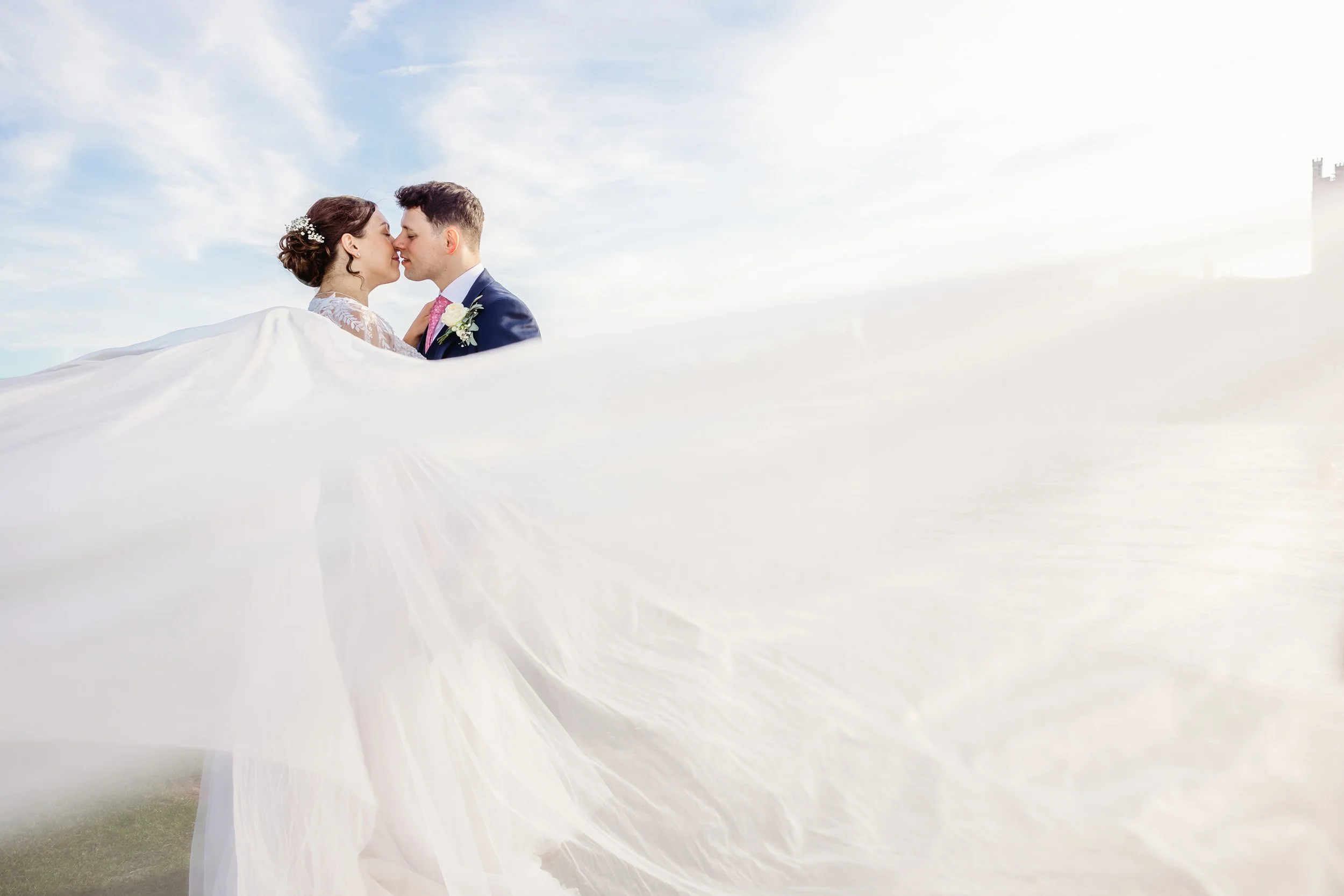 A bride and groom standing close, with their foreheads touching, on a wedding day outdoors under a cloudy sky.