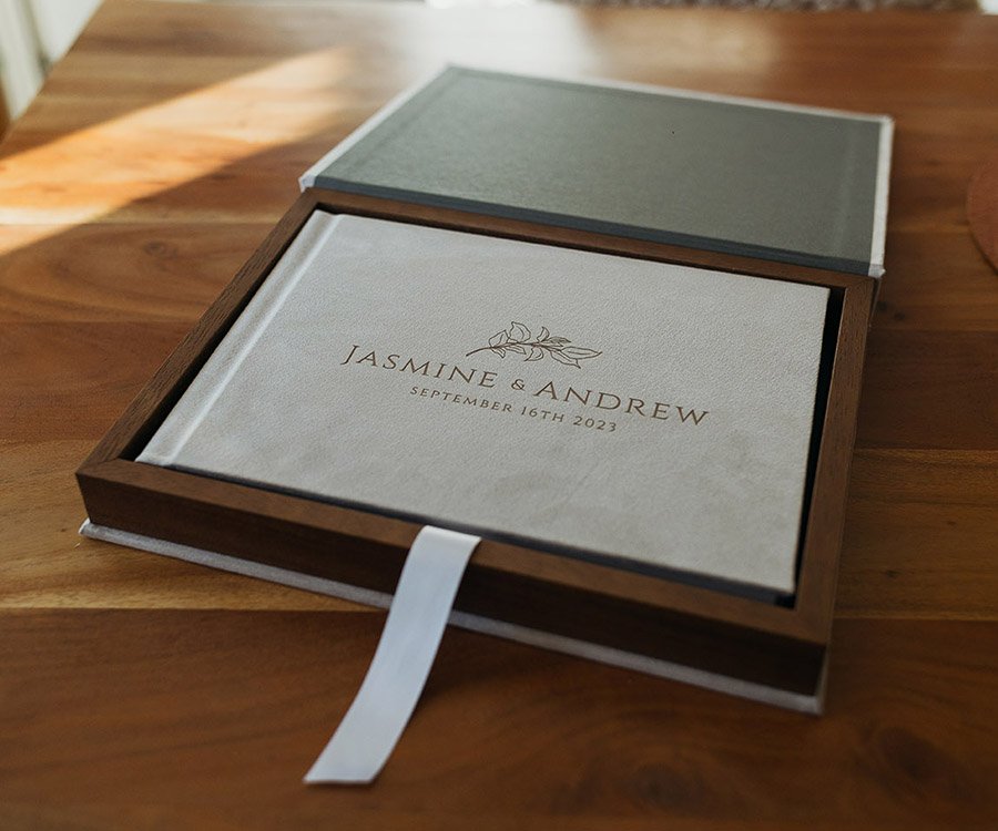 A wedding album with the names Jasmine and Andrew and the date September 16th, 2023, inside a wooden box on a wooden table.
