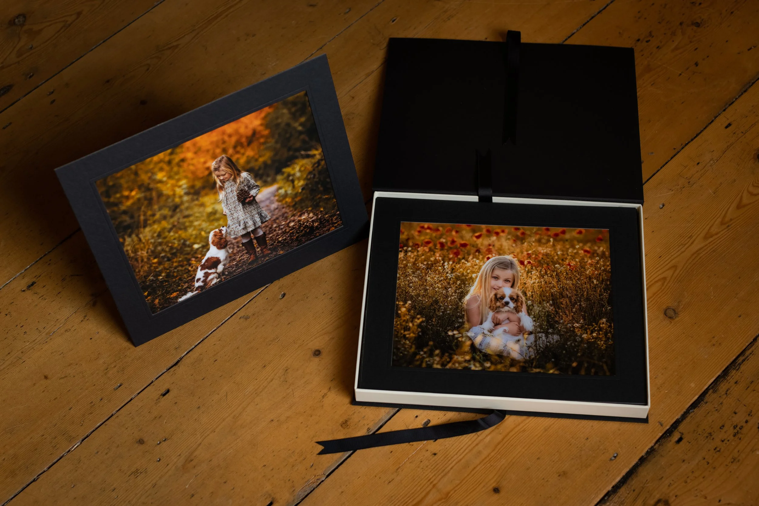 Two framed photographs of children with dogs on a wooden floor, one open and one closed black box