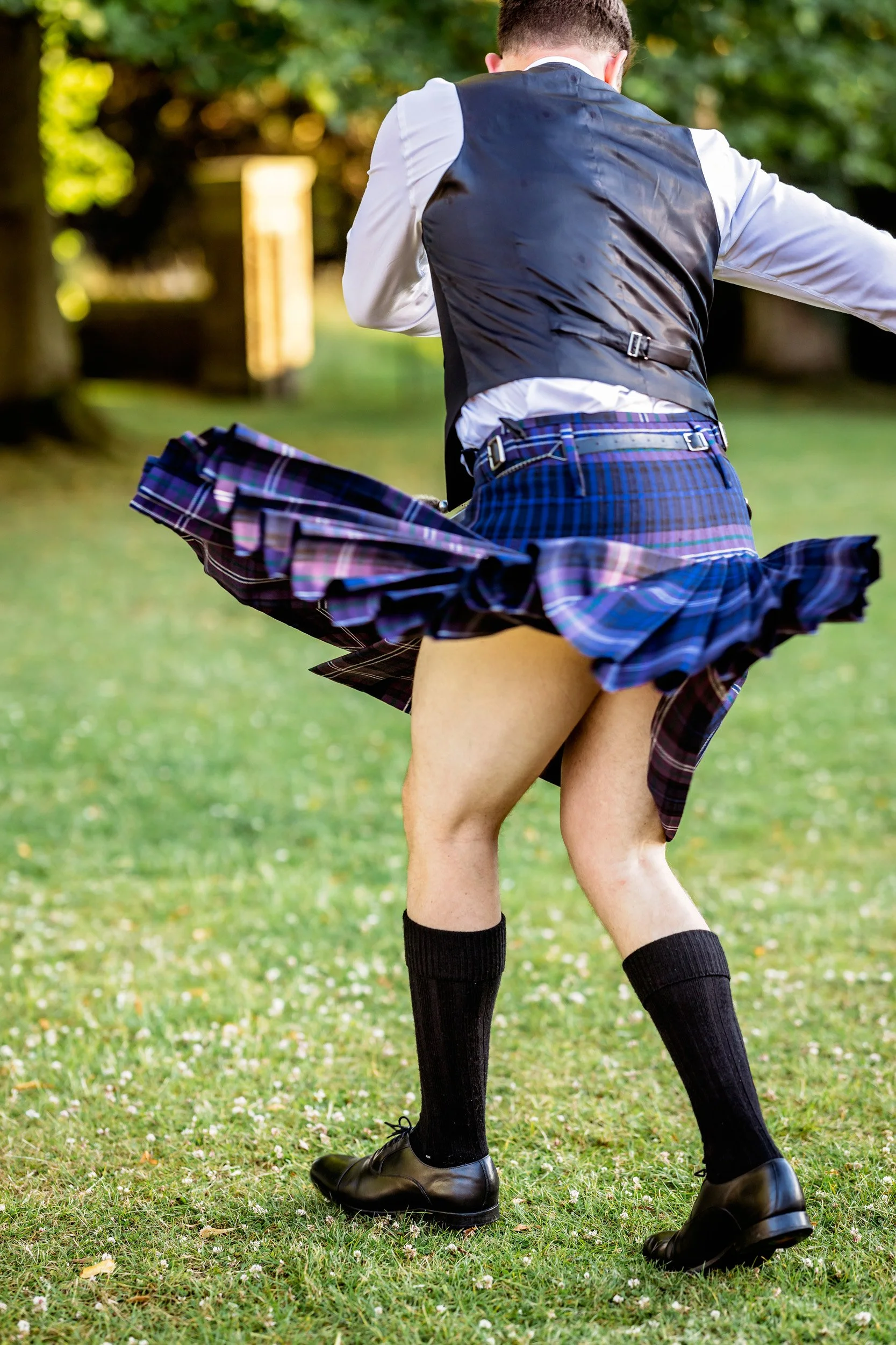 Person dressed in a school uniform with a kilt and knee-high socks, lifting the skirt outdoors.