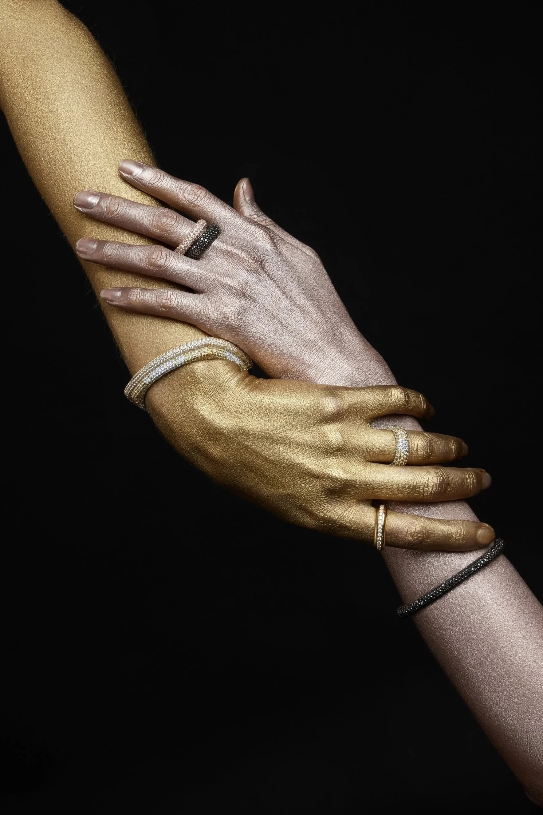 Due mani decorate con smalti oro e rosa, indossano diversi anelli e braccialetti di gioielleria