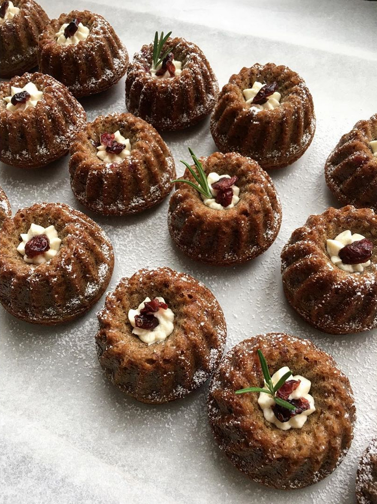 Dolcetti a forma di budino con glassa, decorati con panna, ciliegia secca e rametti di rosmarino, spolverati di zucchero a velo.