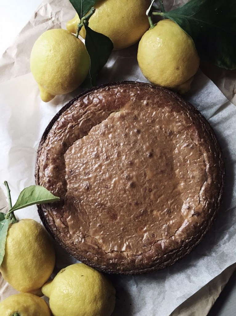 Torta al limone circolare con limoni freschi e foglie intorno.