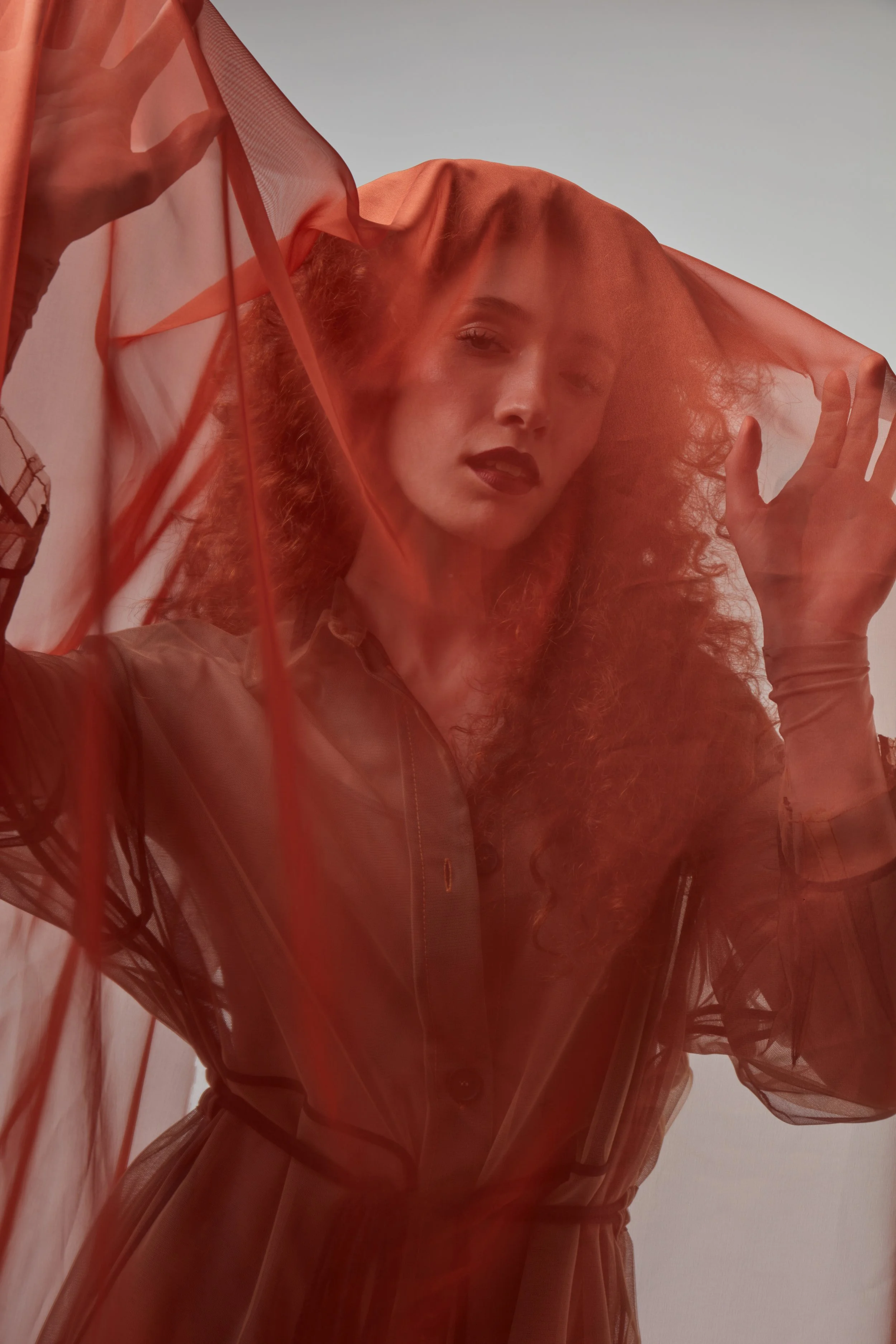 Una donna con capelli ricci rossi, indossa un abito in pelle e tiene una trasparente (rosso) sopra la testa, creando un effetto artistico e d'ispirazione fotografica.