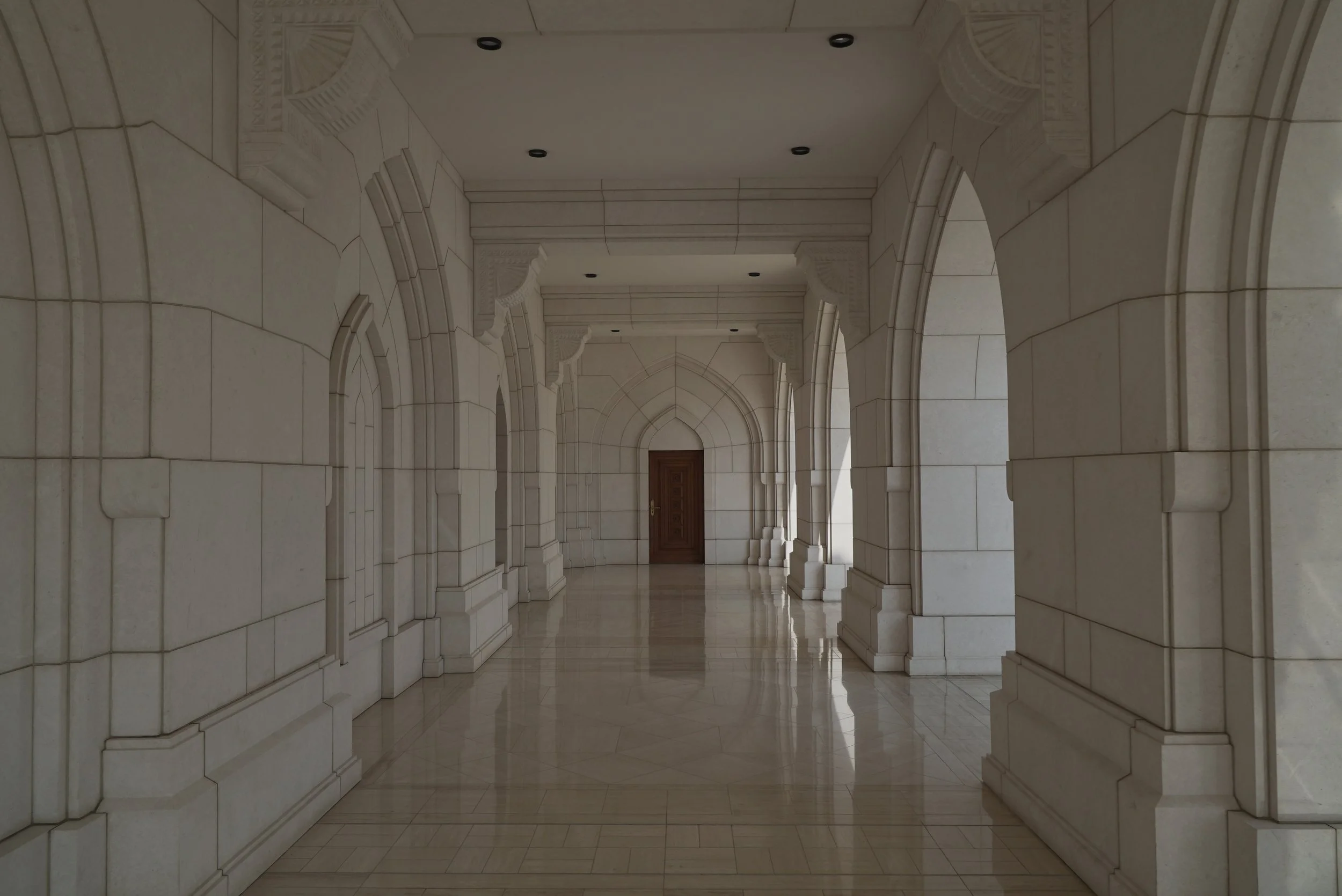 Corridoio interno con archi in pietra chiara, pavimento lucido e porta in legno alla fine.