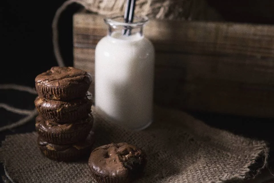 Cinque biscotti al cioccolato impilati e un altro biscotto davanti, con un barattolo di latte e una cannuccia sullo sfondo.