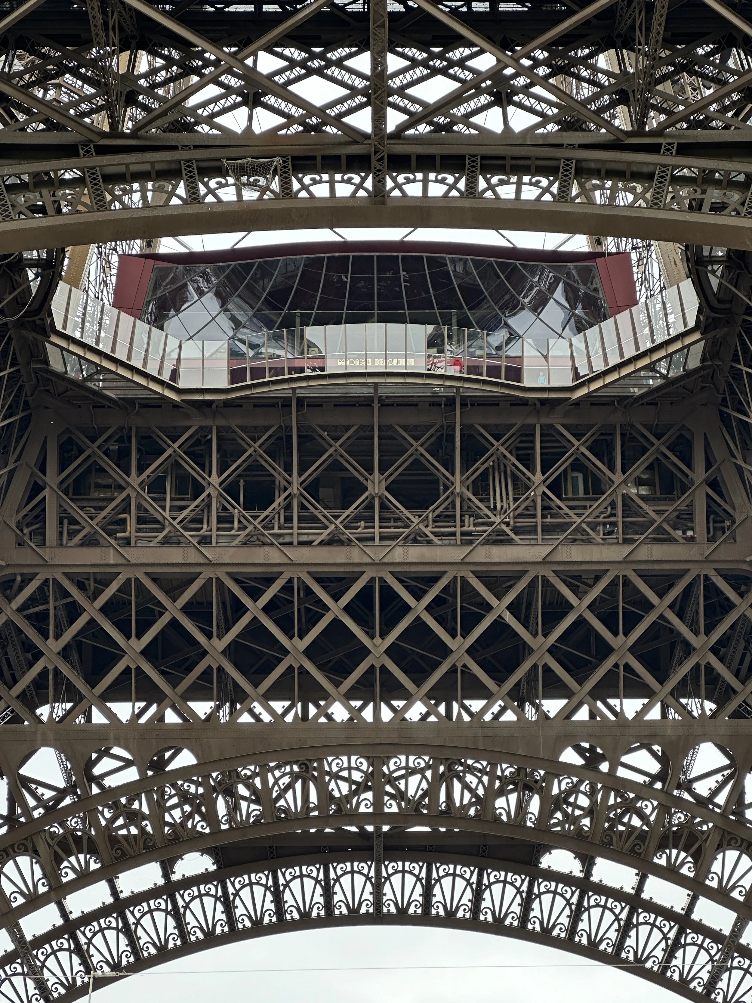 Vista sottostante della struttura in acciaio della Torre Eiffel a Parigi, con dettagli delle sue travi e piattaforme.