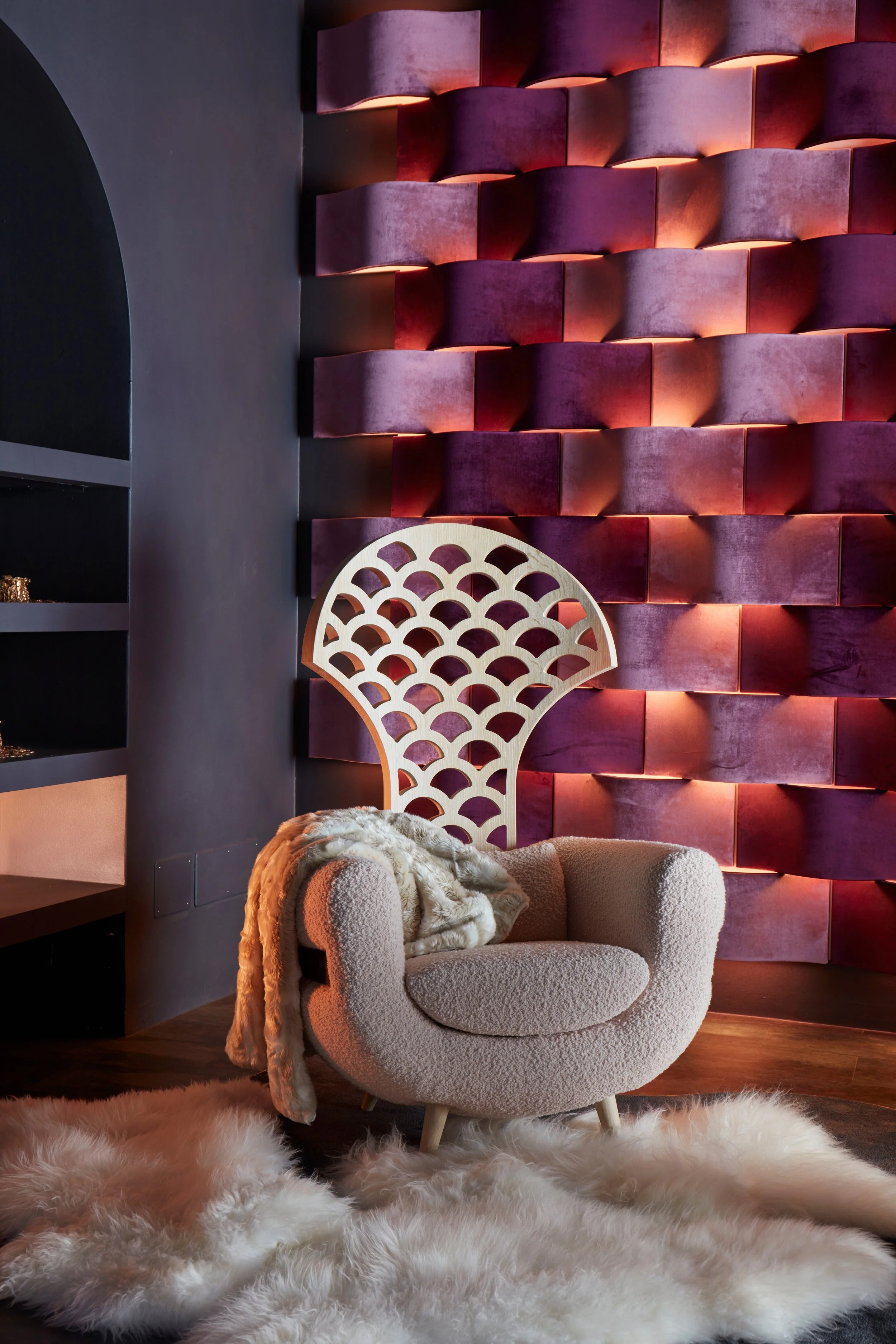 Soggiorno con sedia decorativa, poltrona bianca in tessuto morbido, tappeto bianco peloso e parete rossa con illuminazione ambientale.