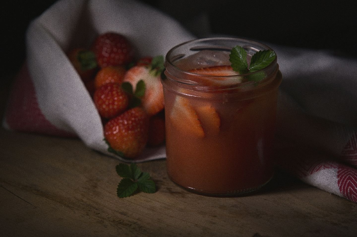 Barattolo di limonata con fette di limone e foglie di menta, accanto a fragole fresche, tutto su un piano di legno.