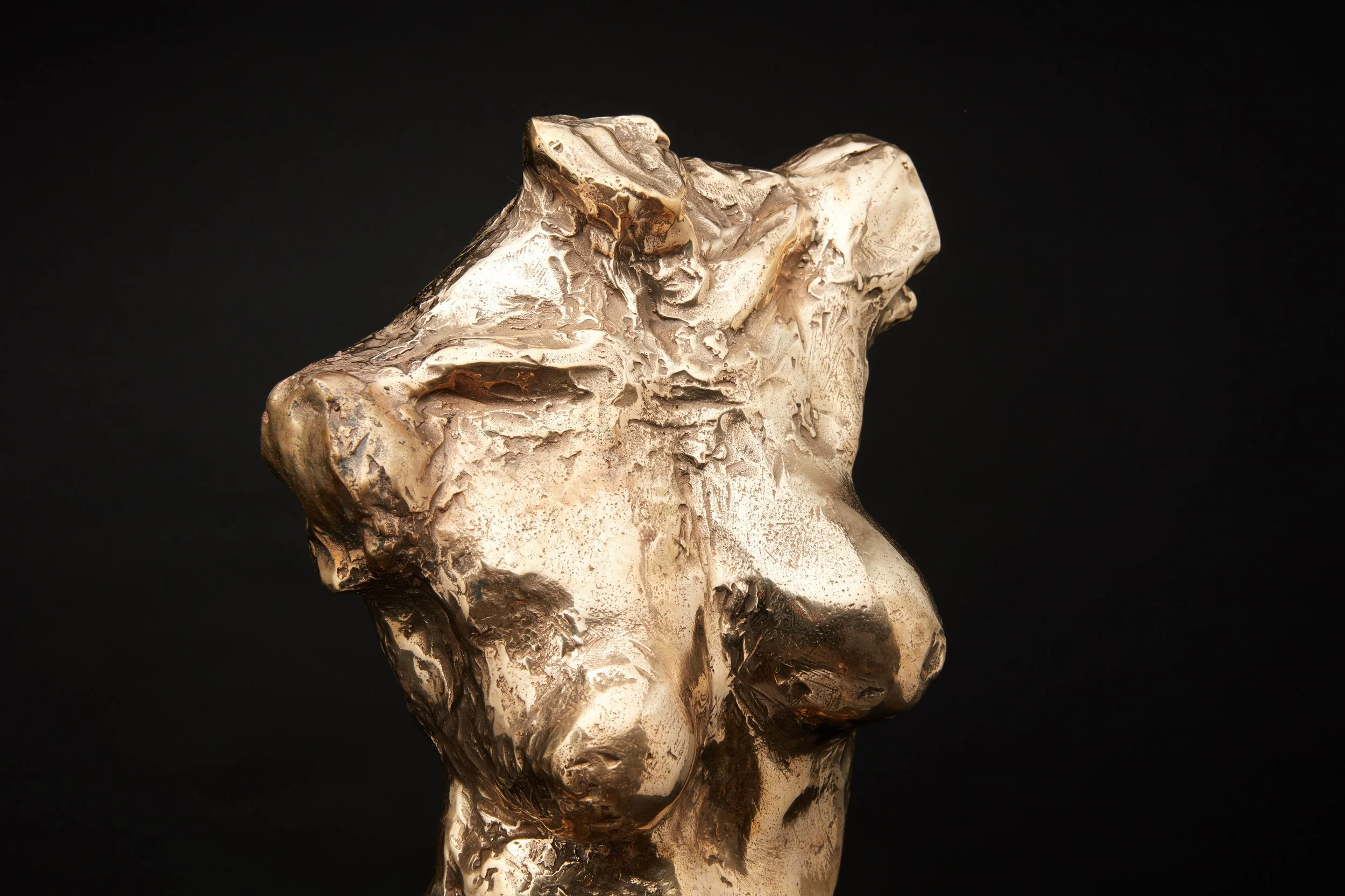 Scultura astratta in metallo con superficie irregolare e lucida, rappresenta un volto stilizzato, contro uno sfondo nero.