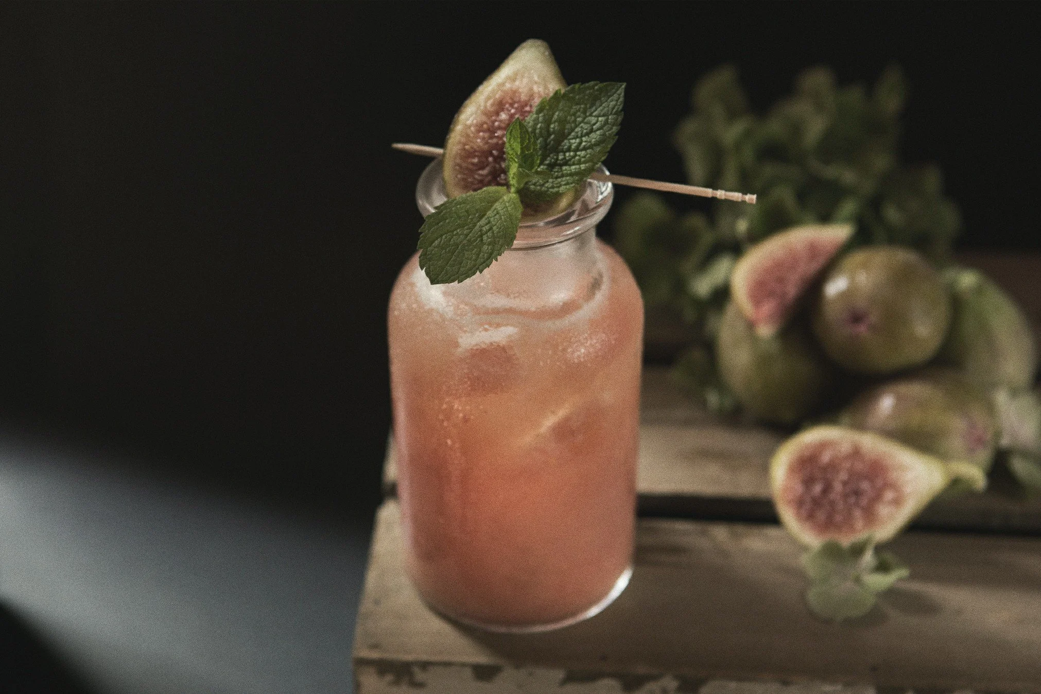 Bottiglia di cocktail rosa con menta e fichi come decorazione e fuscelli di fichi accanto