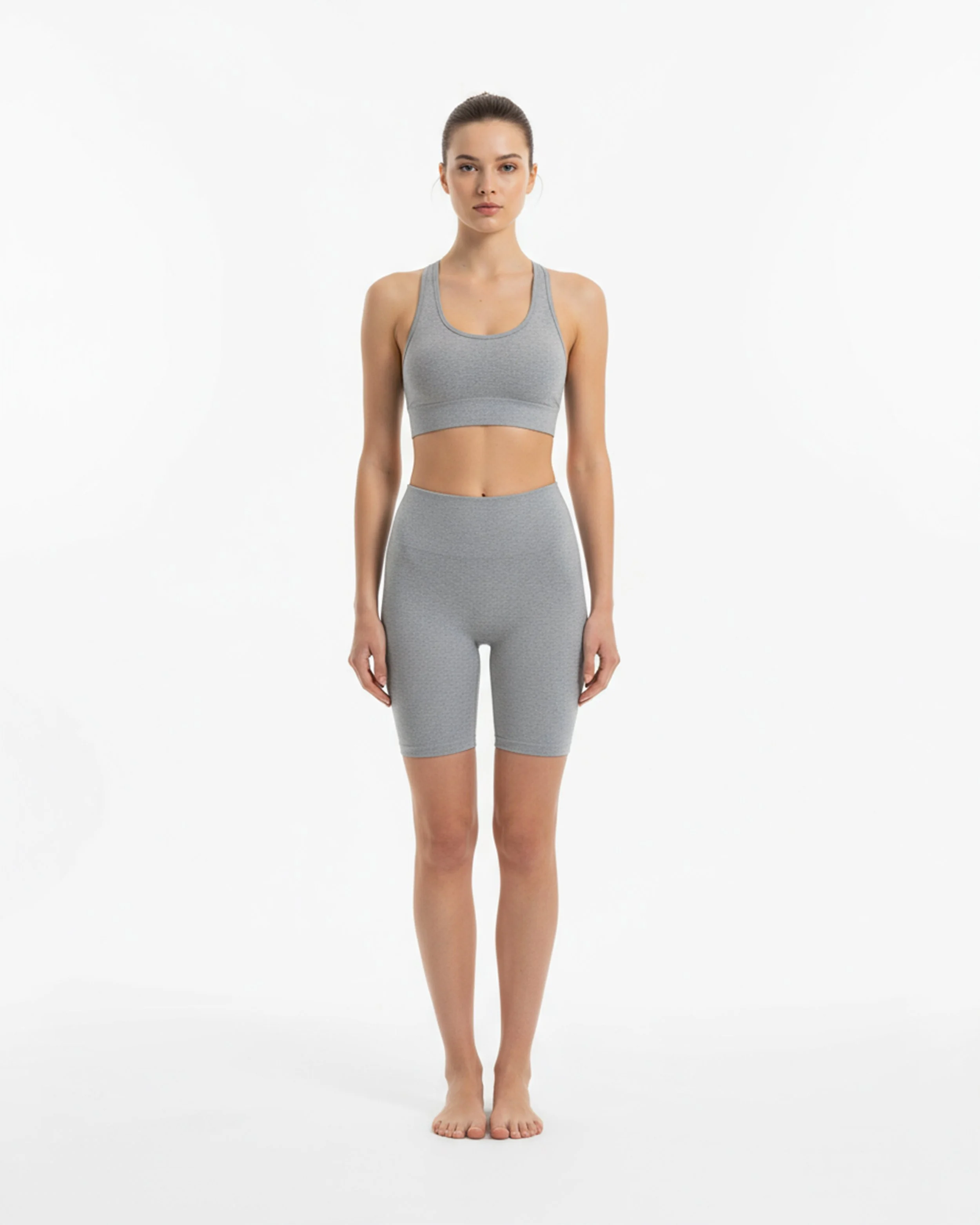 Donna in abbigliamento sportivo grigio che si prepara per un allenamento su sfondo bianco.