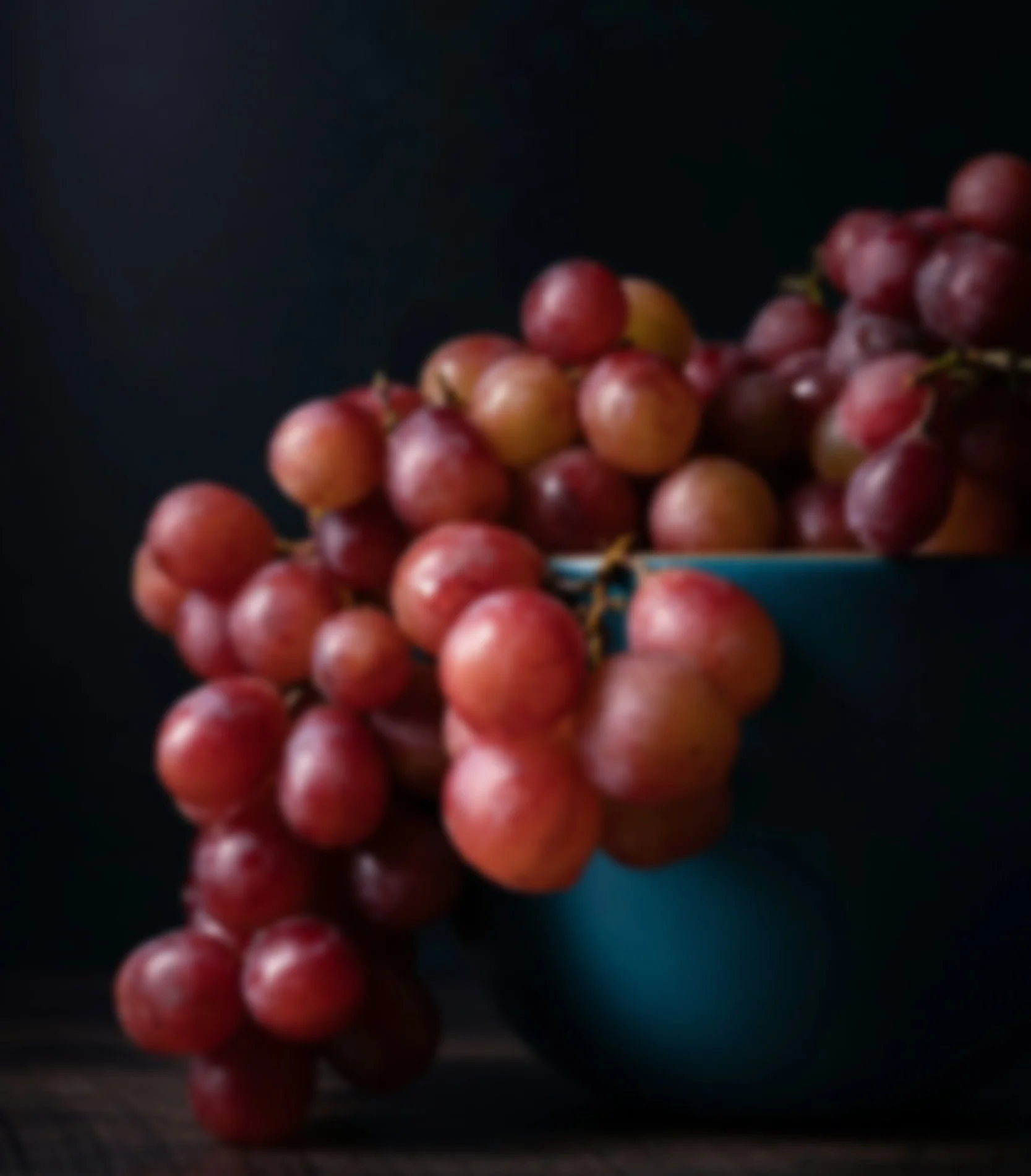 Uva rossa in una ciotola blu scuro contro sfondo nero.