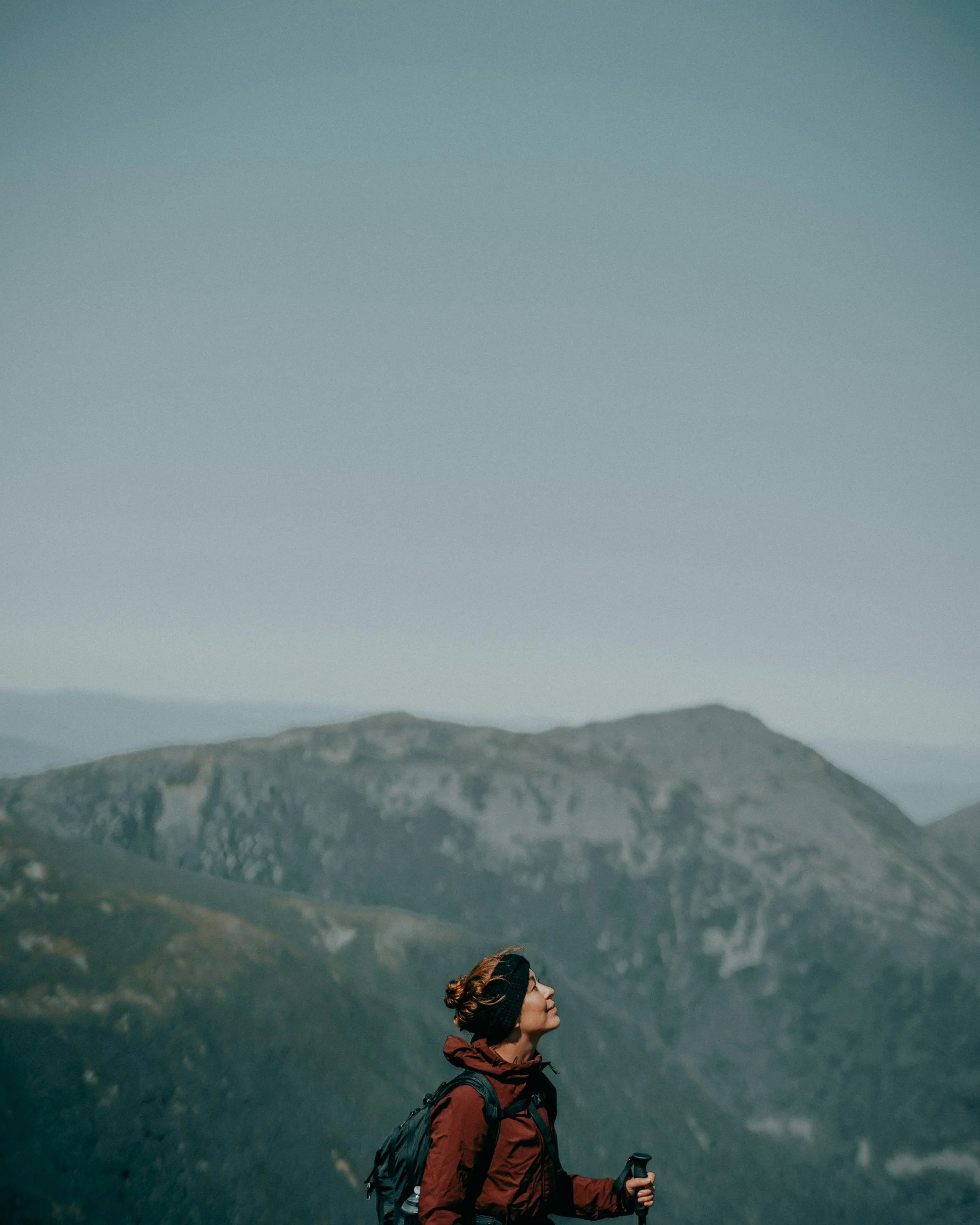 Image of woman wearing rust-colored hiking jacket hiking in a mountain range