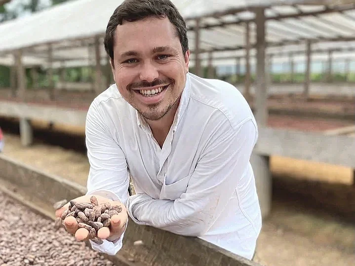 Maxime Pliester, founder of Concept chocolate. A man smiling and holding a handful of cocoa beans in a greenhouse.
