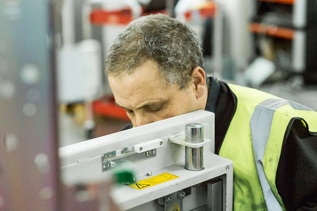 A man in a yellow safety vest examining machinery in an industrial or manufacturing setting.