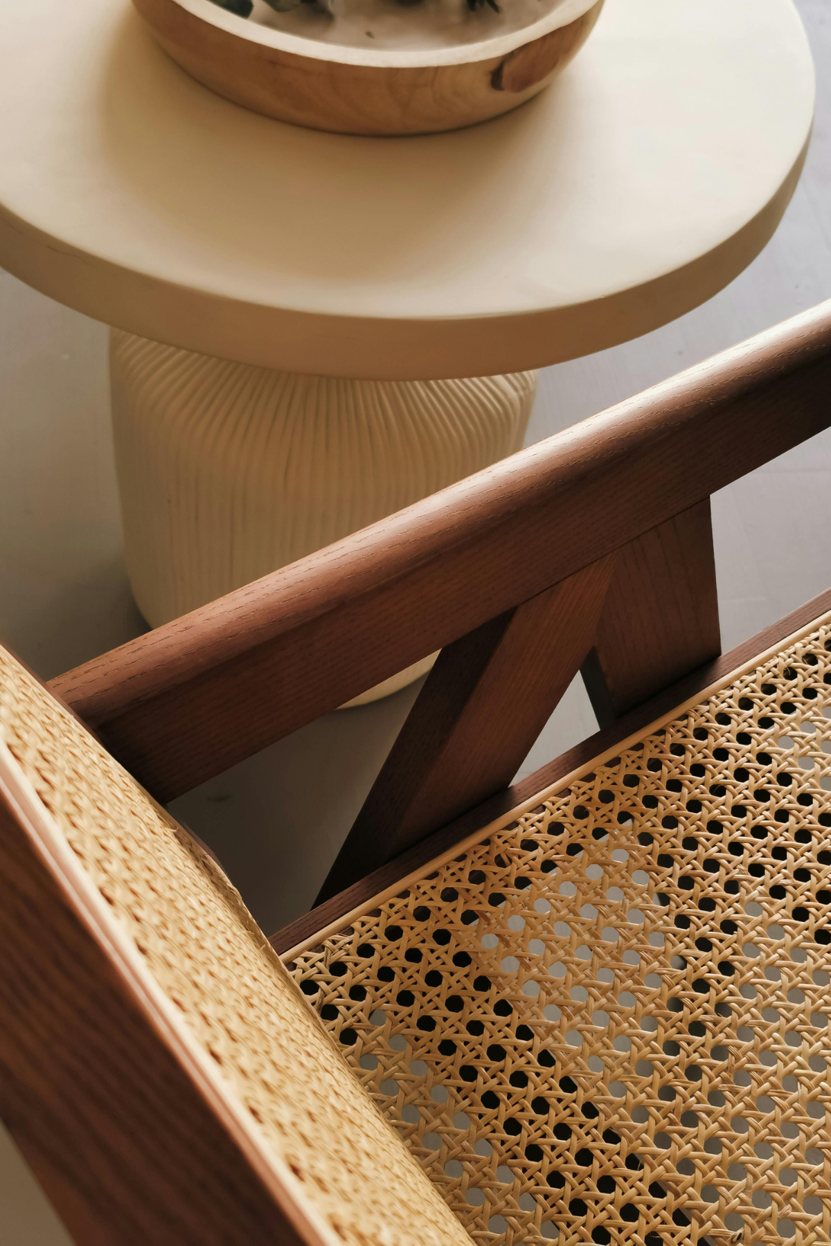 Vue en plongée d'une table ronde en bois clair avec un vase blanc en arrière-plan, et une chaise en bois avec un dossier en cannage.