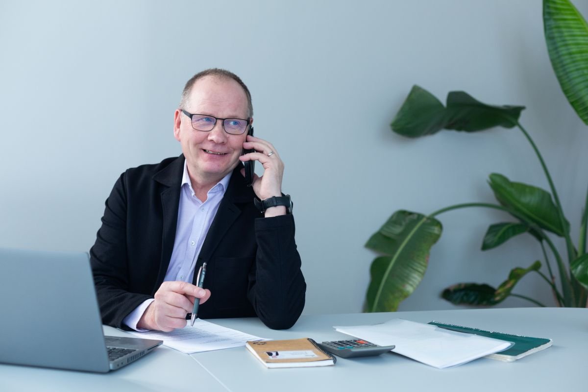 Mikko Rautiainen puhelimessa tietokoneen äärellä. Pöydällä muistikirja ja papereita.