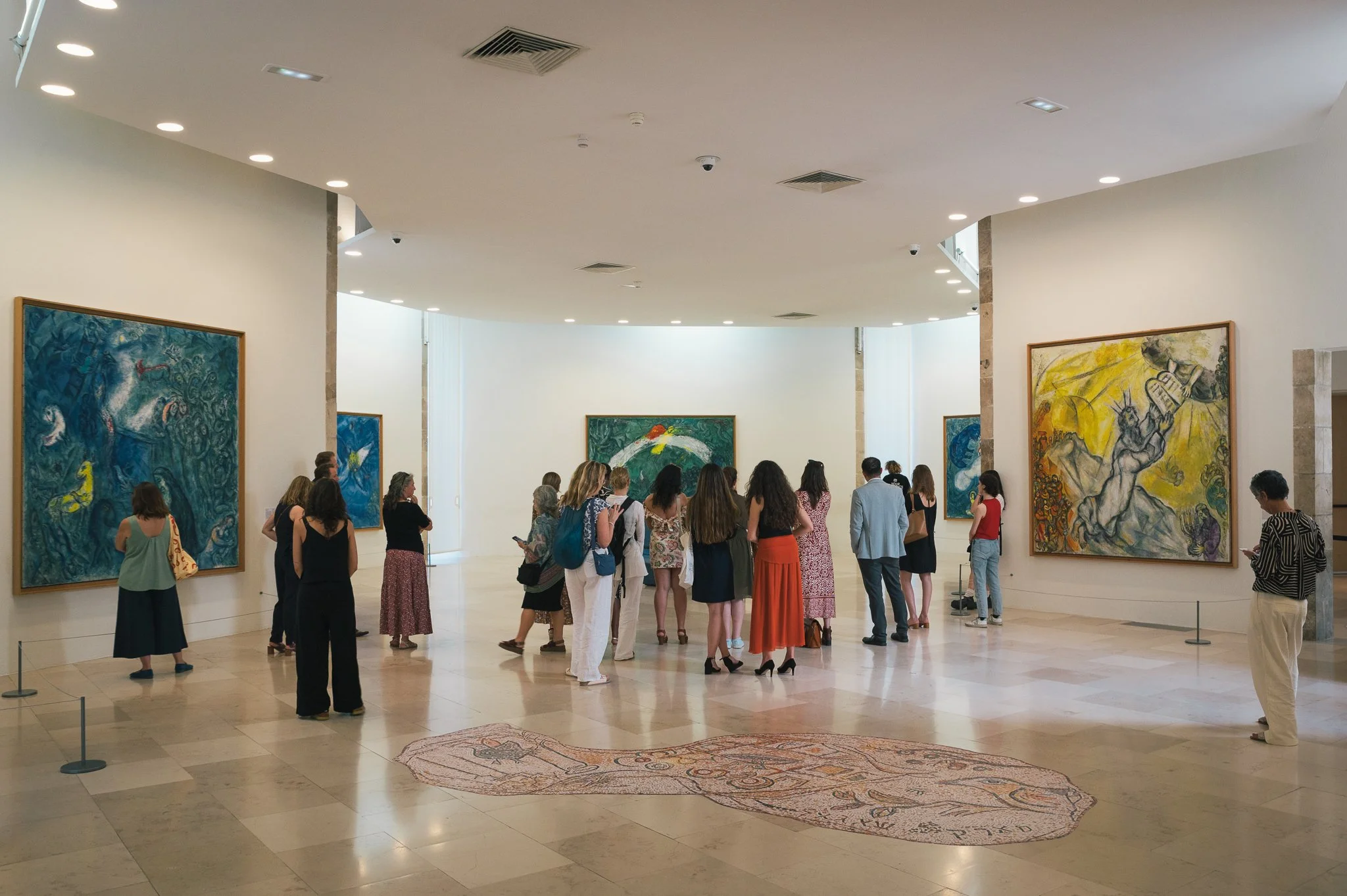 A group of people in an art gallery viewing colorful paintings on the walls.