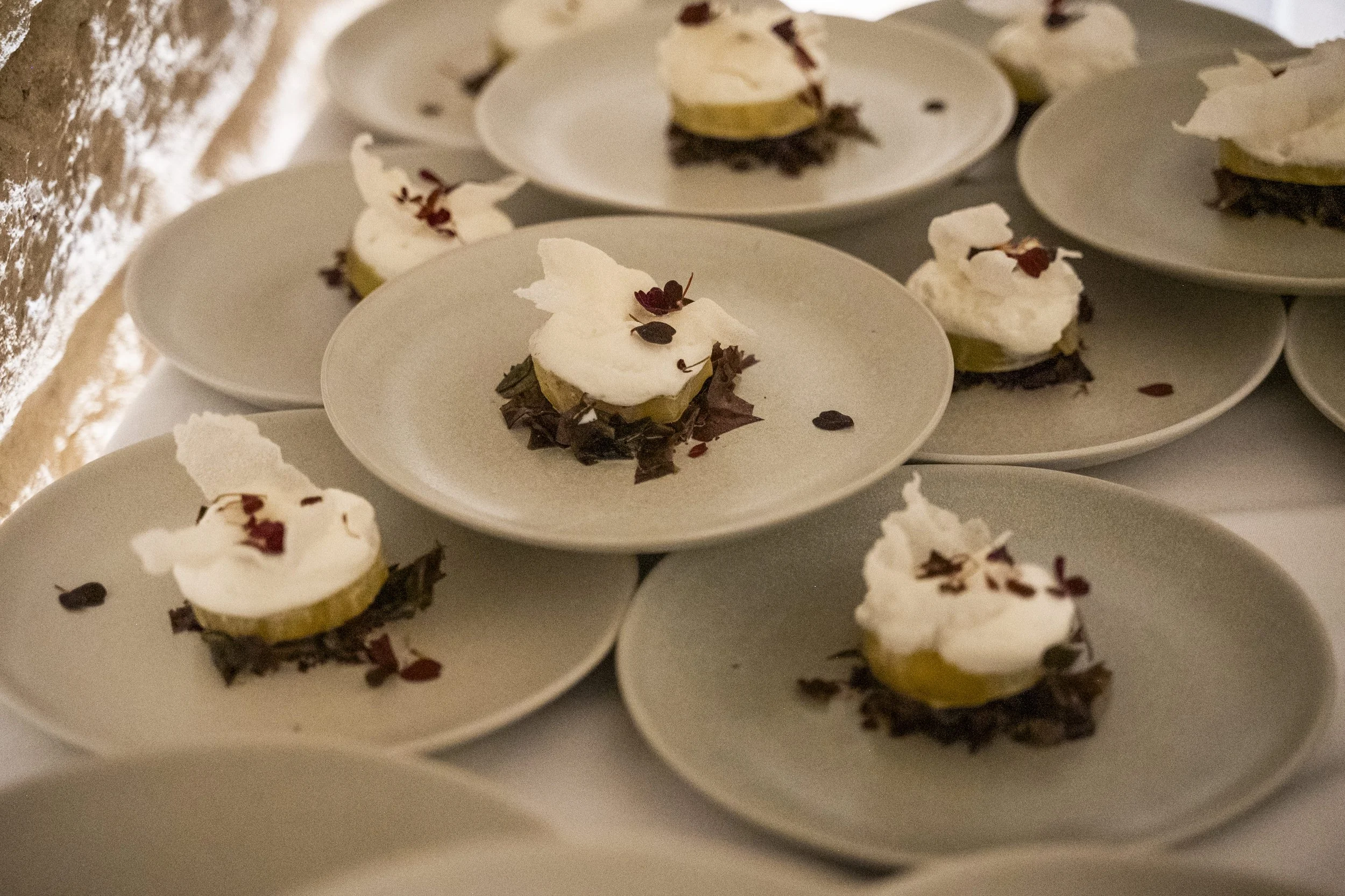 Elegant dessert plates with layered sweets topped with whipped cream, garnished with small red and dark chocolate pieces, and placed on a white tablecloth.
