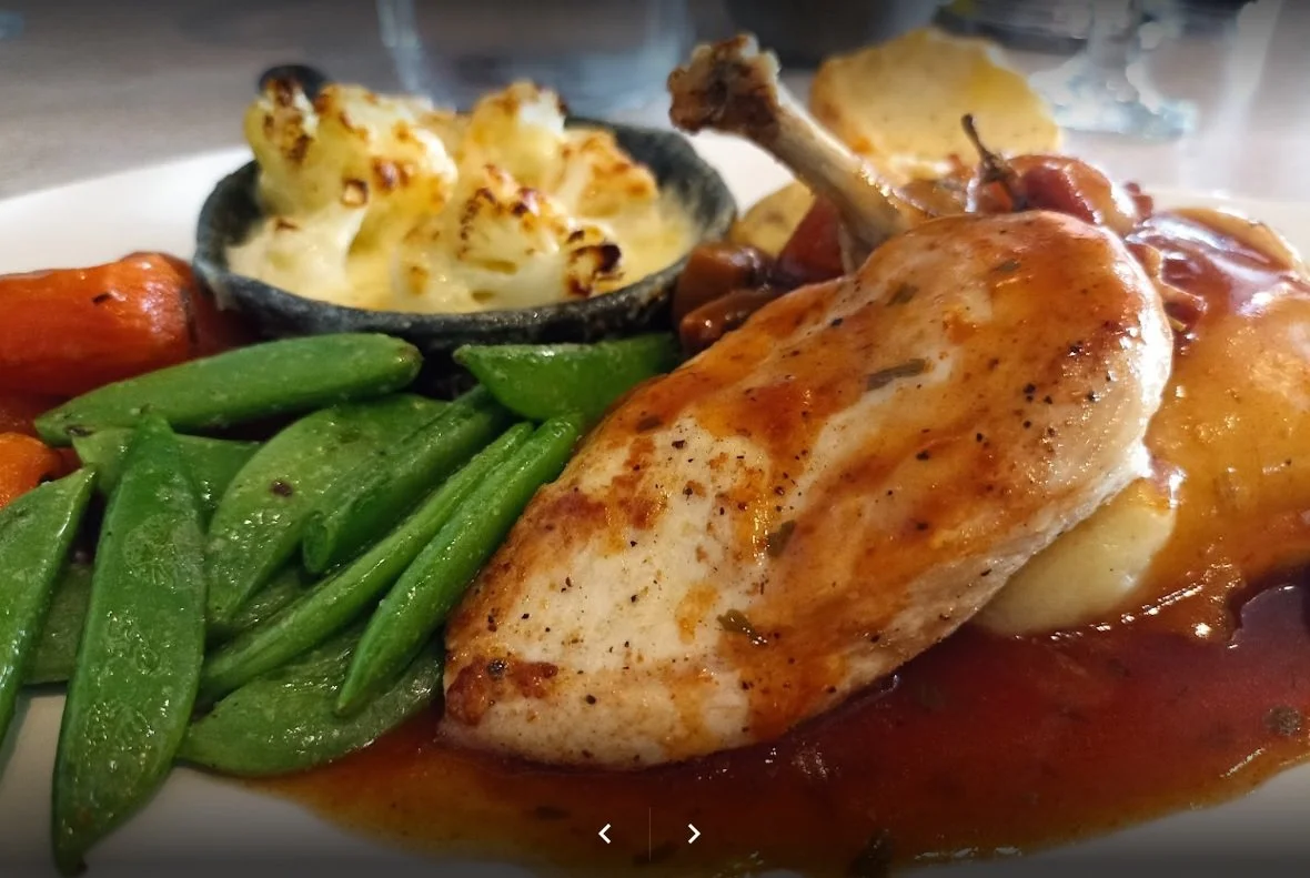 Cooked chicken thigh with gravy, green beans, roasted carrots, and mashed potatoes with browned topping.