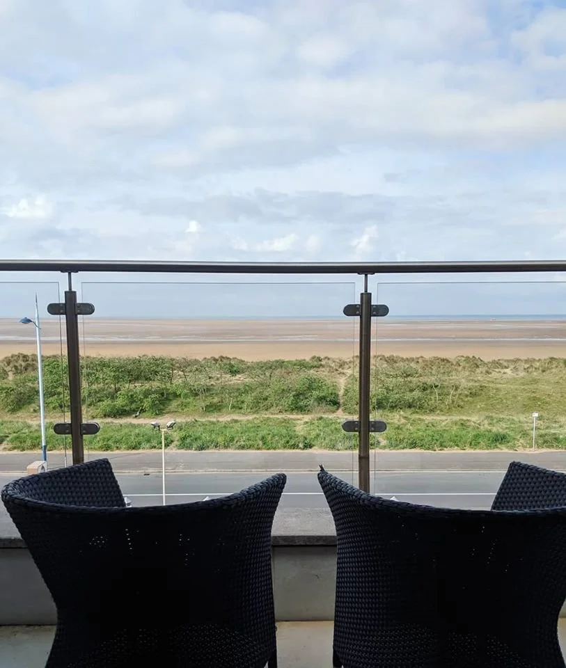 Balcony with two black wicker chairs overlooking a beach and open sky.